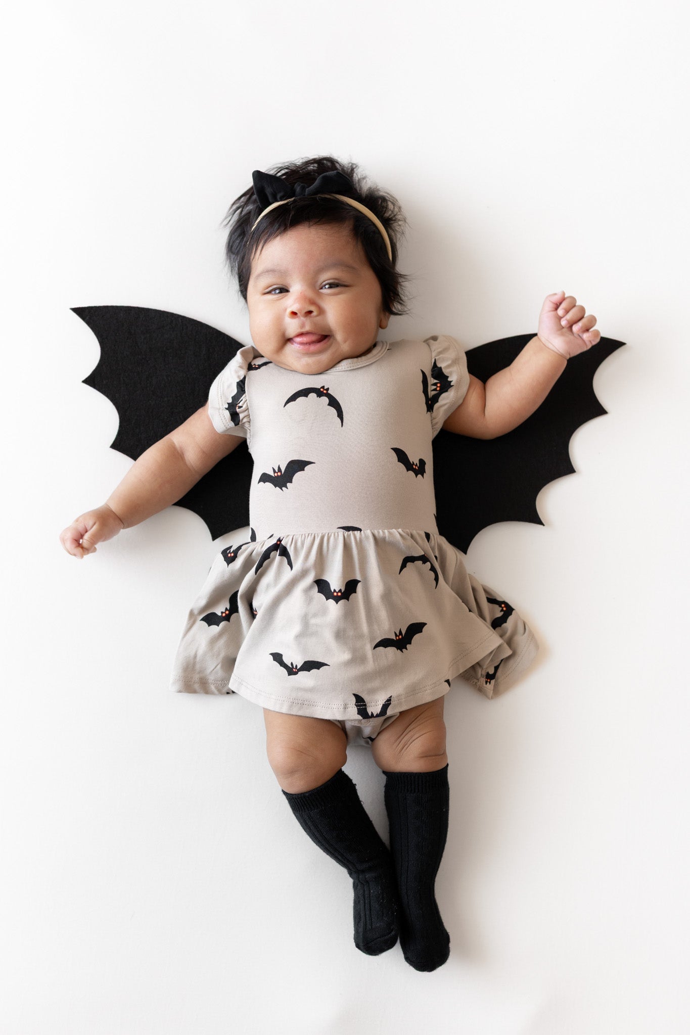 Baby wearing Twirl Bodysuit Dress in Bats print with bat wings and black socks on a white background