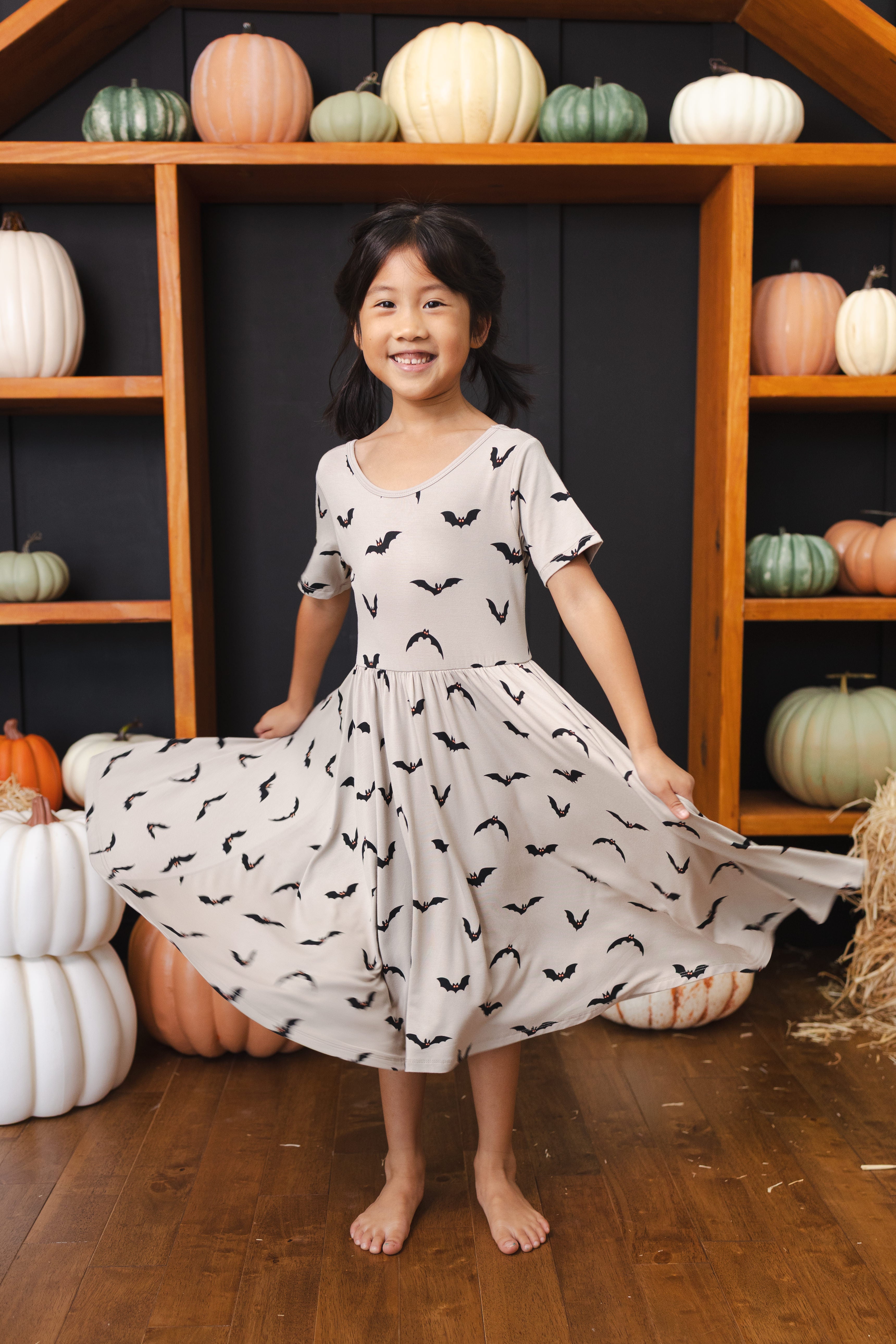 Girl in Twirl Dress in Bats print smiling in front of pumpkin decorations