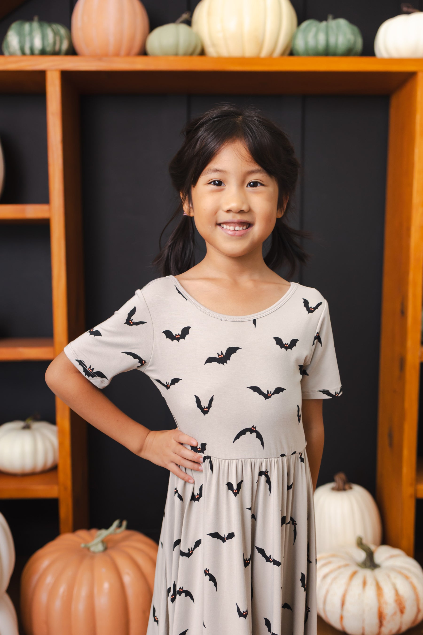 Close up of Girl wearing Twirl Dress in Bats print smiling in front of pumpkin decorations