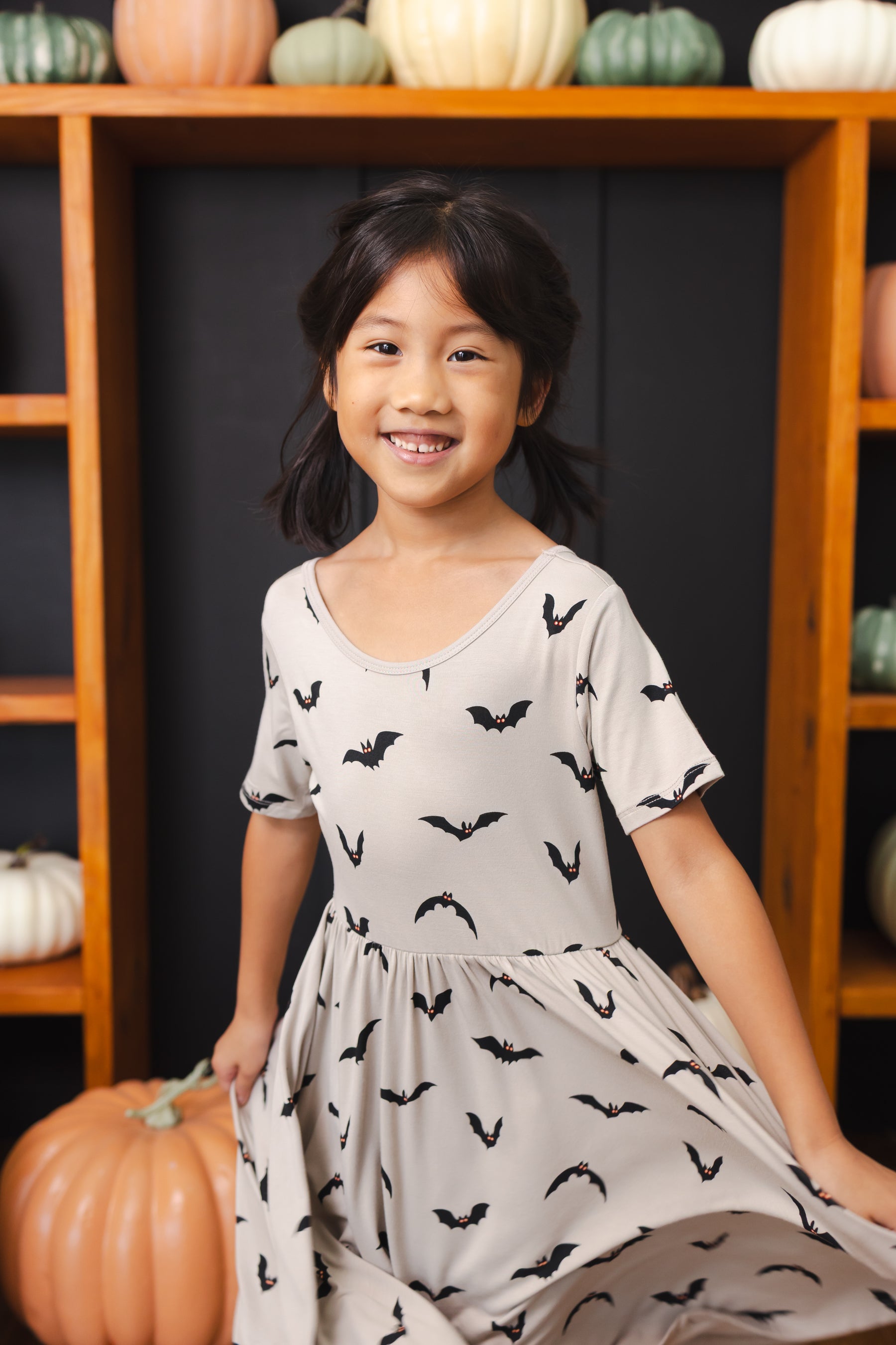 Girl wearing Twirl Dress in Bats print smiling in front of pumpkin decorations