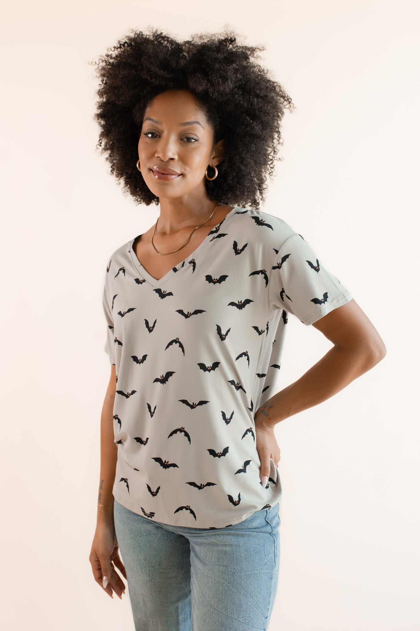 Modal posing in Women's Oversized V-Neck Tee in Bats print over light blue jeans on a beige background