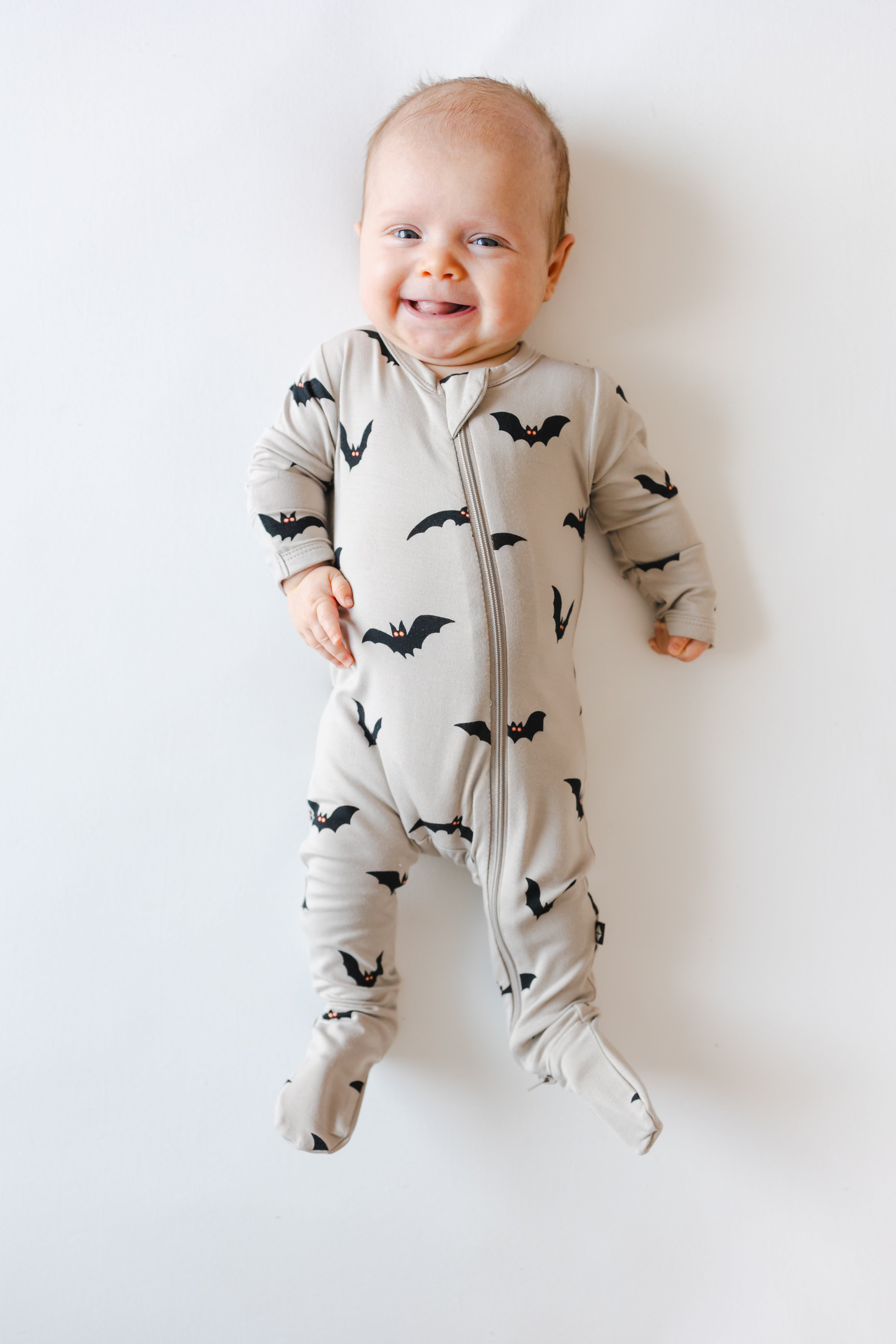 Baby smiling in Zippered Footie in Bats print on a white background