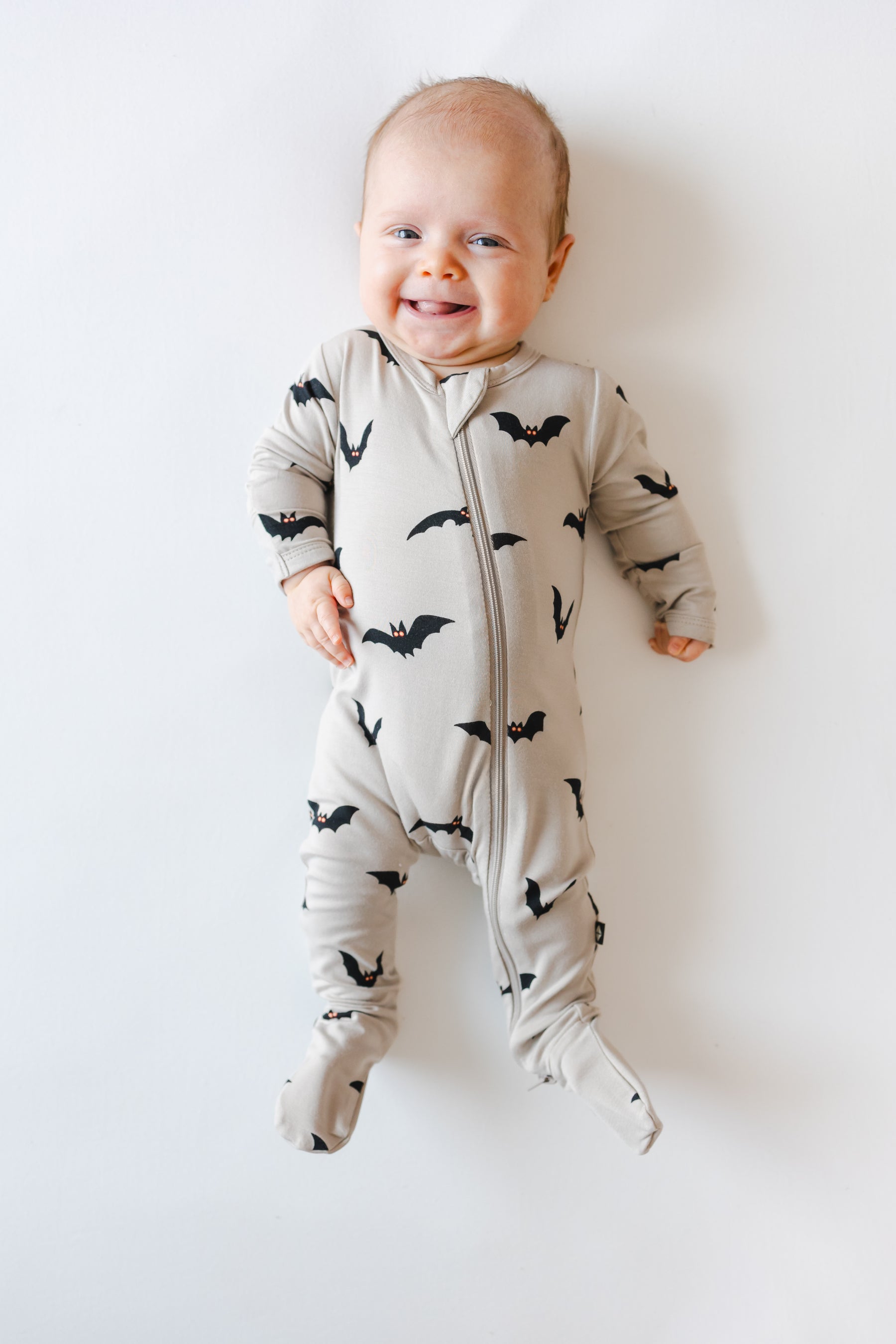 Baby smiling in Zippered Footie in Bats print on a white background