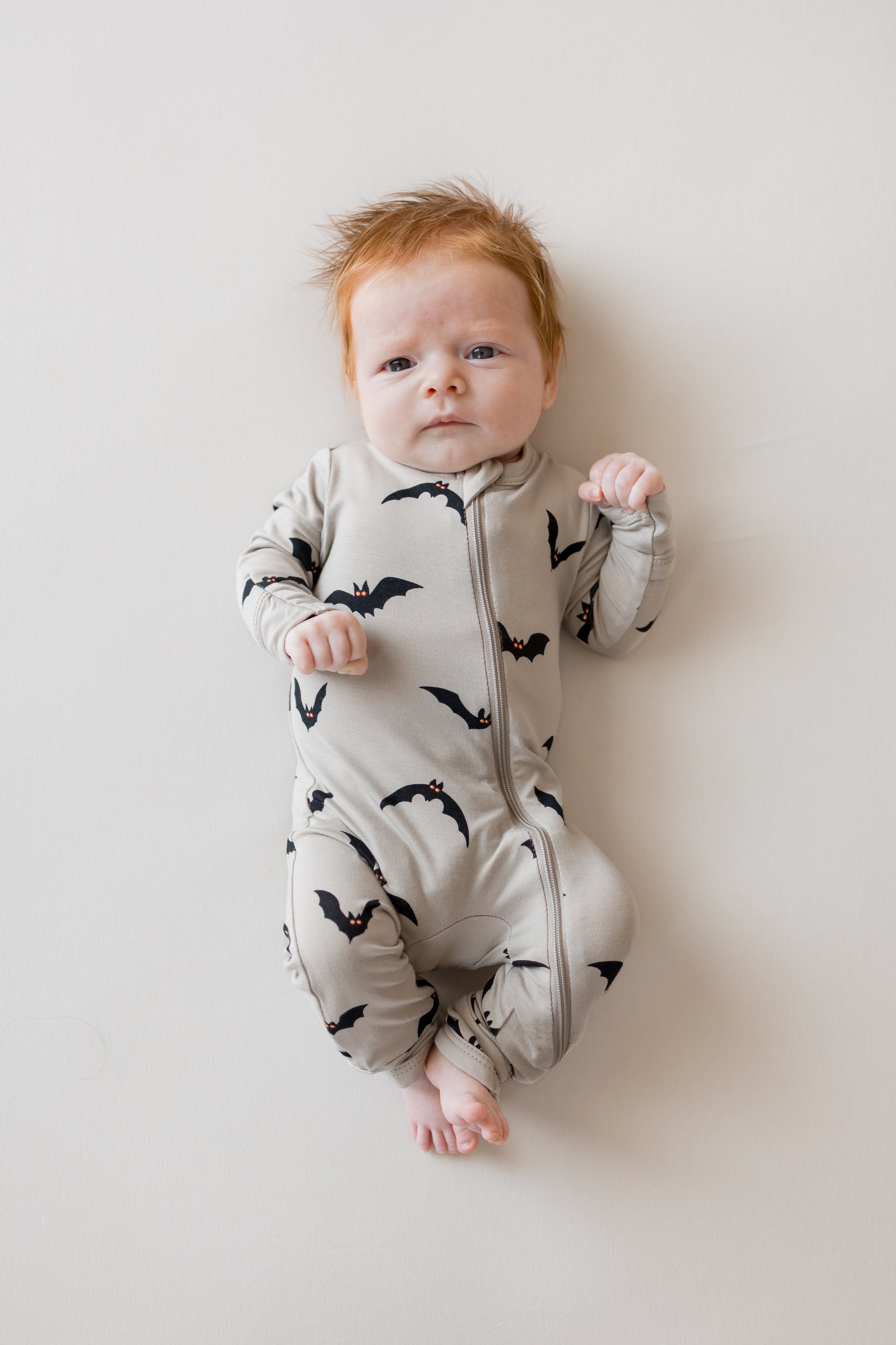 Baby wearing zippered romper in Bats print on a beige background