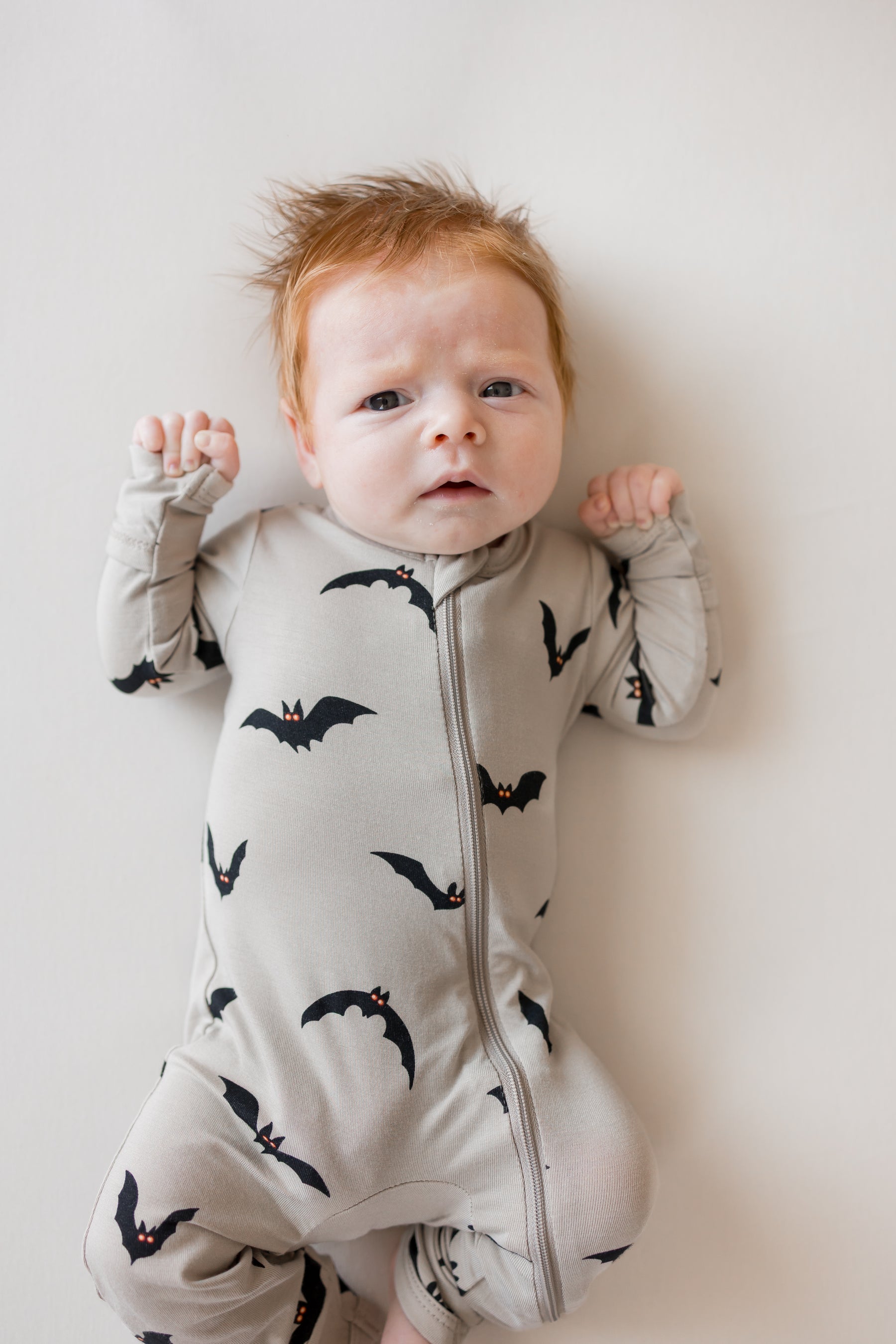 Baby wearing zippered romper in Bats print on a beige background