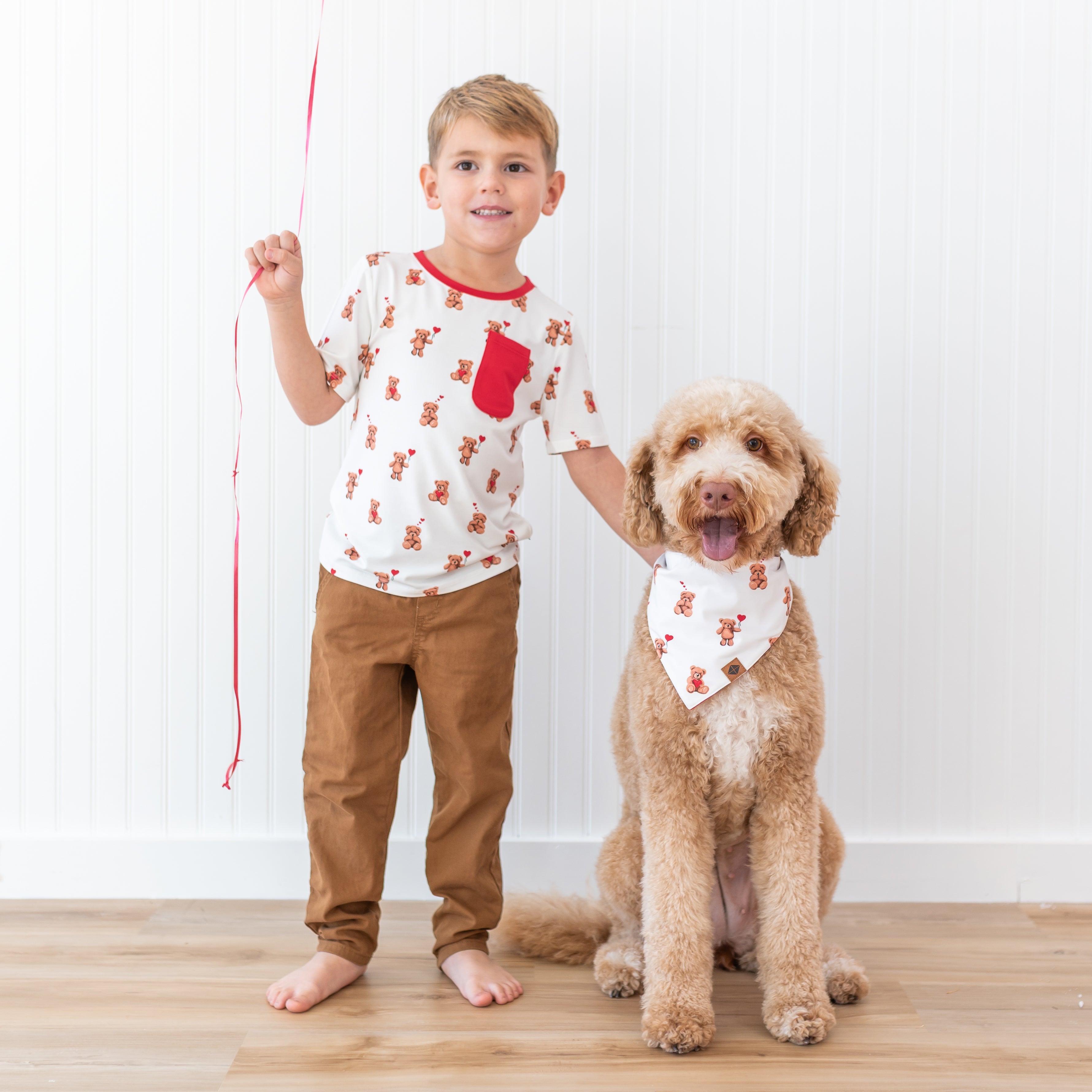 Smiling boy wearing the short sleeve crew neck in Bear hearts standing beside a medium dog wearing the Dog Bandana in Bear Hearts