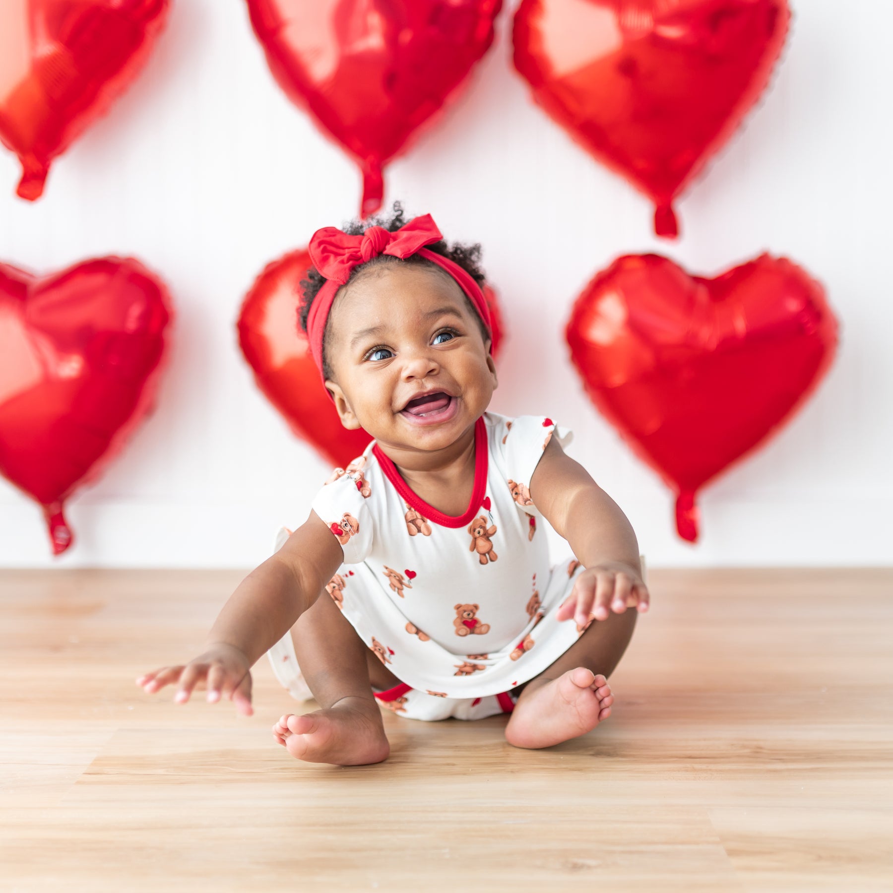 Toddler sitting on the floor wearing the Twirl Bodysuit Dress in Bear Hearts paired with a cardinal knotted bow headband