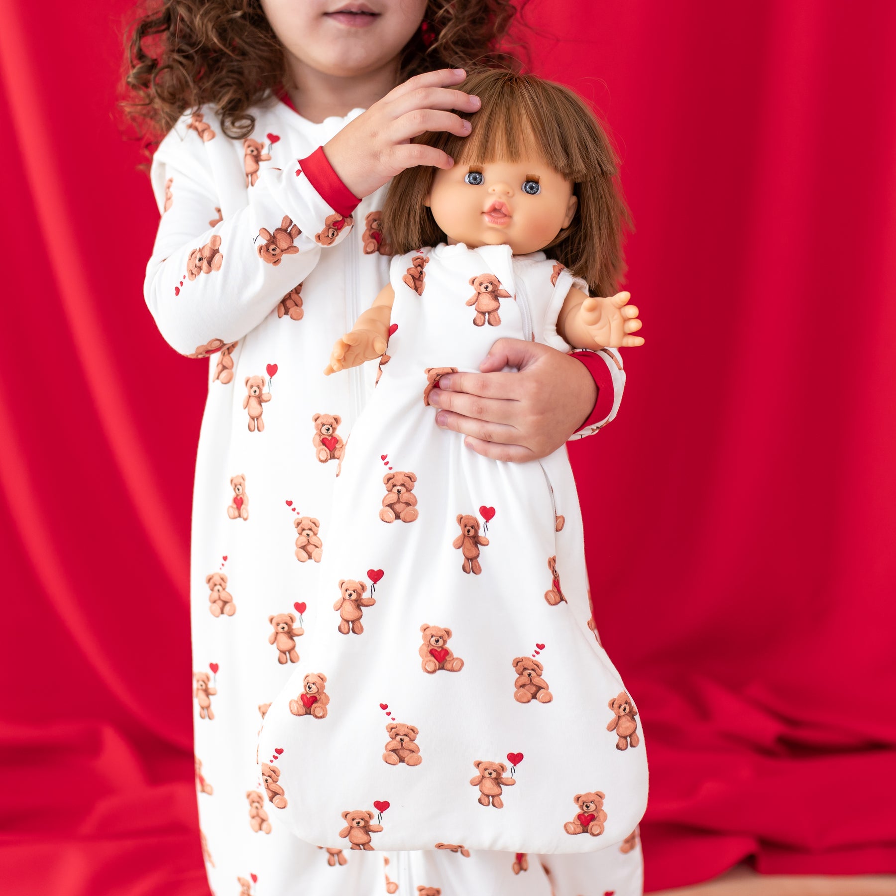 Toddler girl earing the Sleep Bag walker in Bear hearts holding a doll wearing a matching Baby Doll Sleep Bag in Bear Hearts