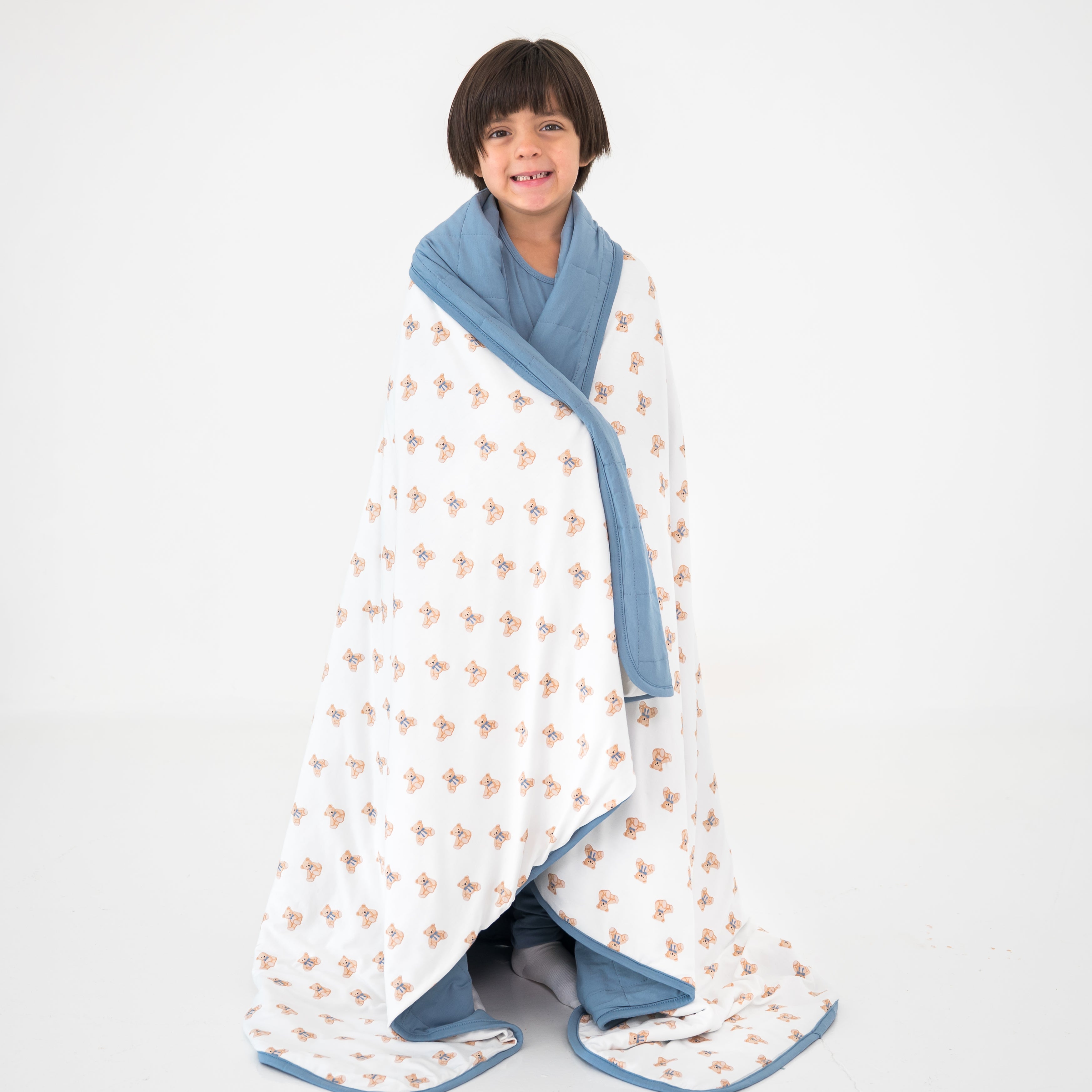Child wrapped in a teddy bear pattern blanket with blue trim on a white background