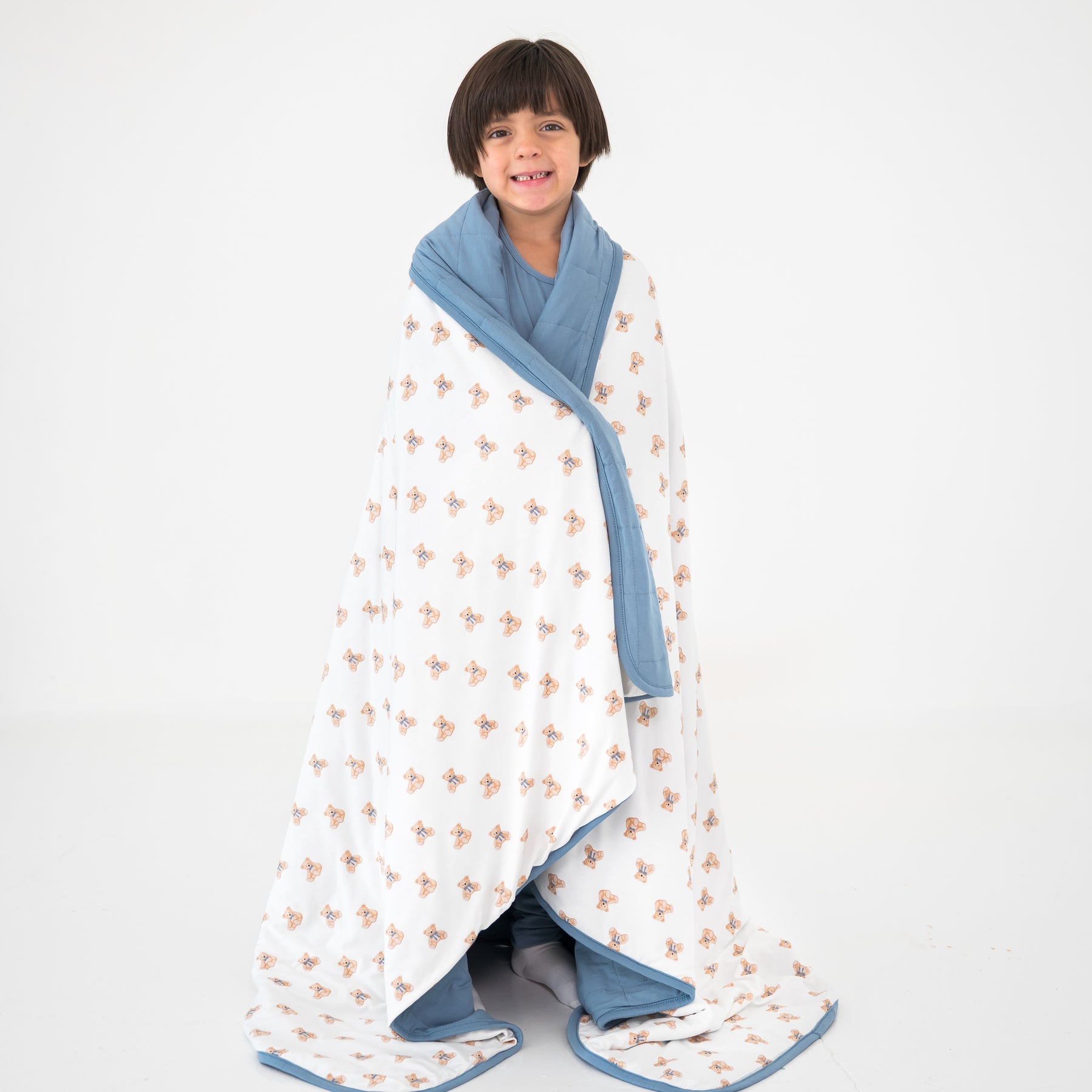 Child wrapped in a teddy bear pattern blanket with blue trim on a white background