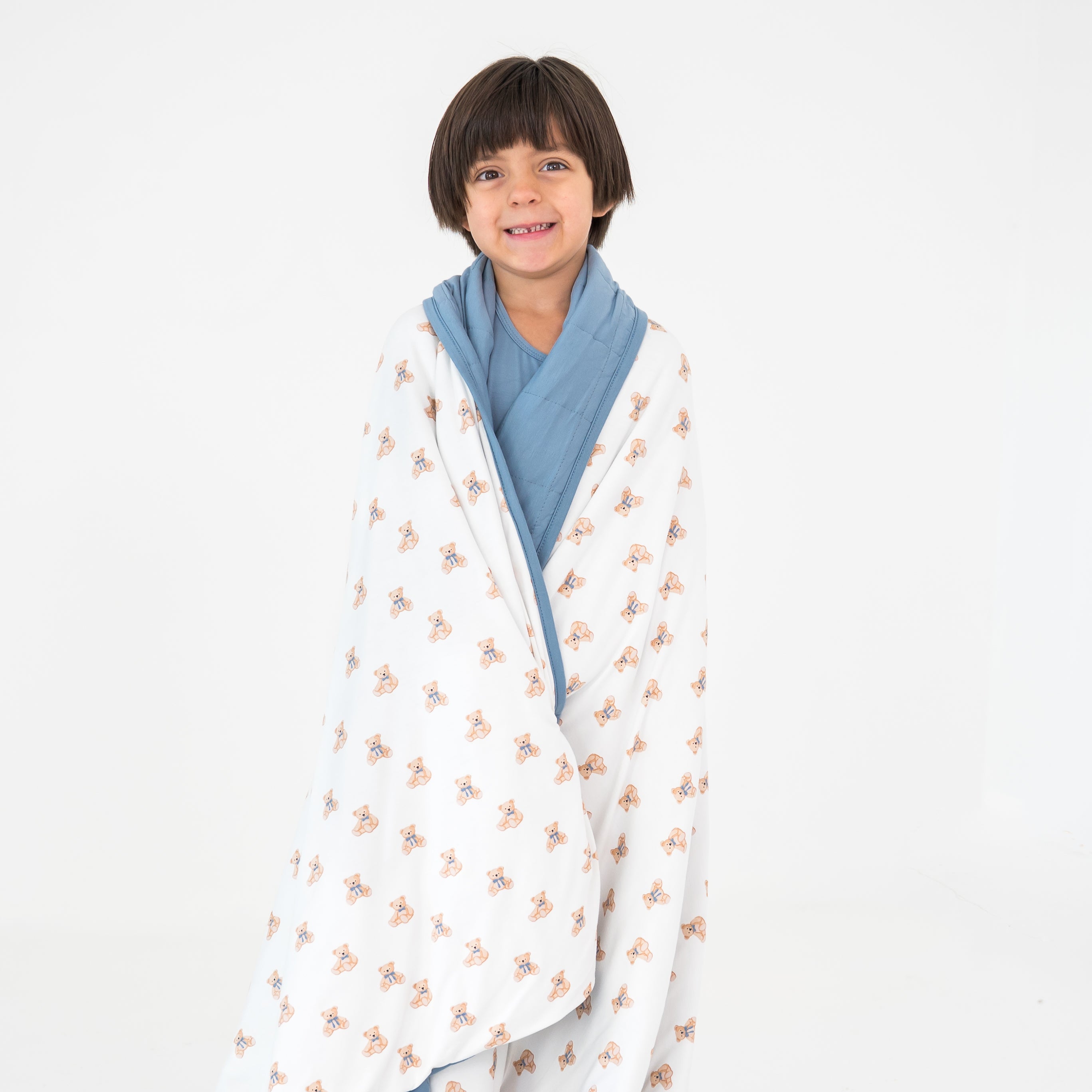 Child wrapped in a bear patterned blanket with blue trim on a white background