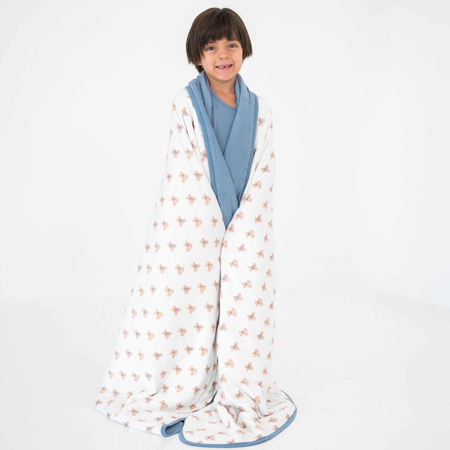 Child wrapped in a teddy bear patterned blanket with a plain background