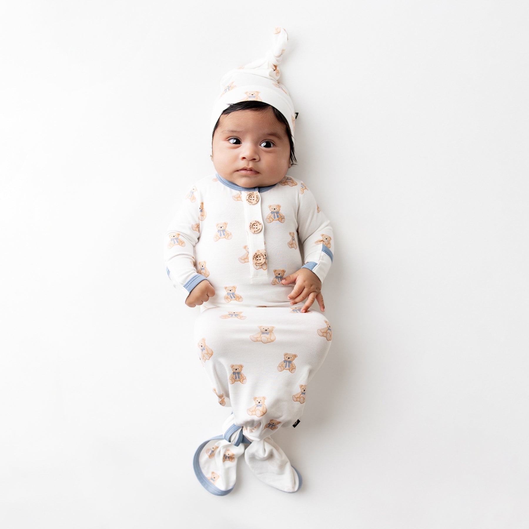 Infant laying on a flat white surface wearing the Knotted Gown with Hat Set in Teddy Bear