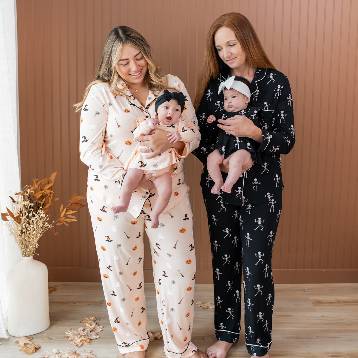 Two women wearing matching pajama sets with baby girls on a wooden floor.