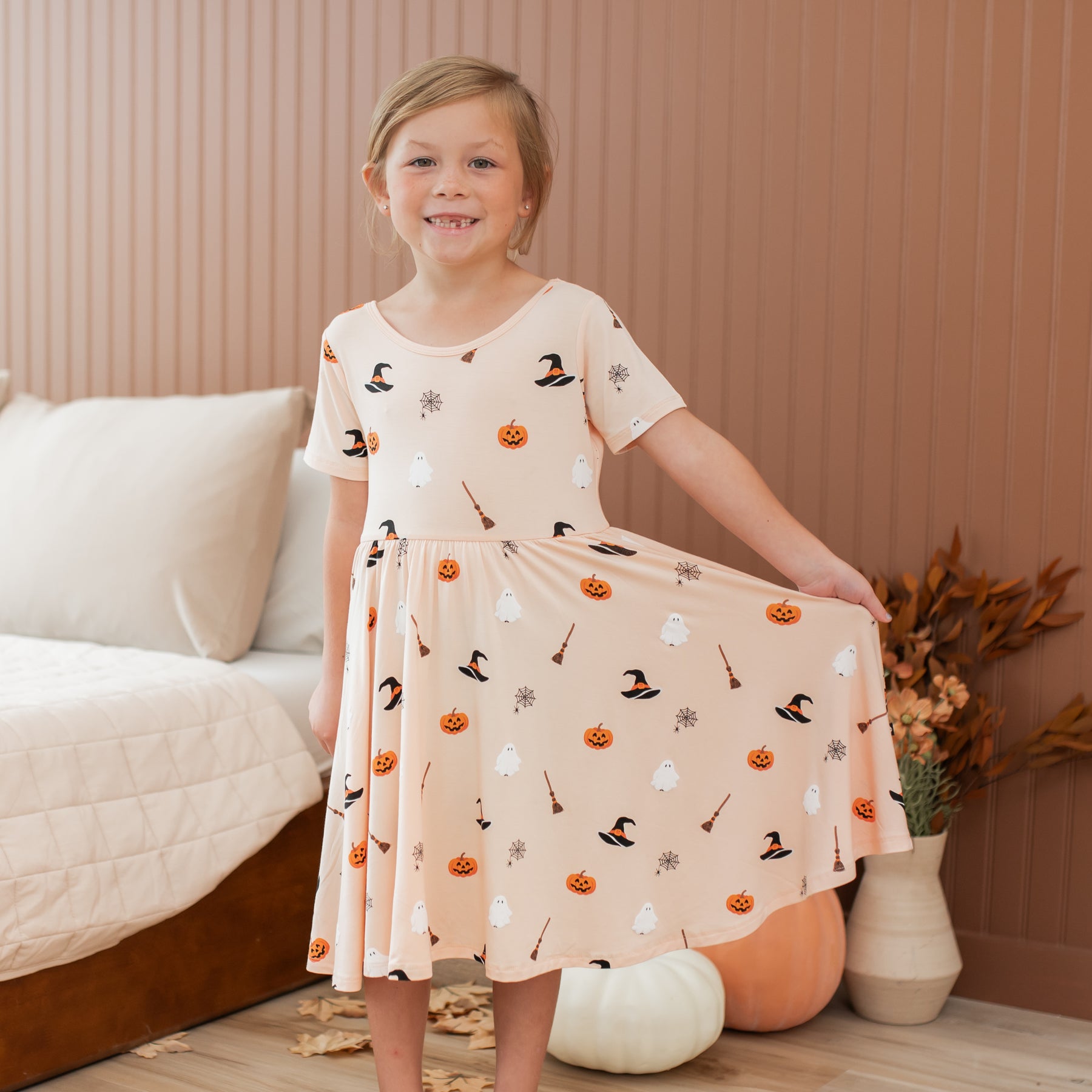 Young girl wearing a Halloween-themed peach colored dress in a cozy room.
