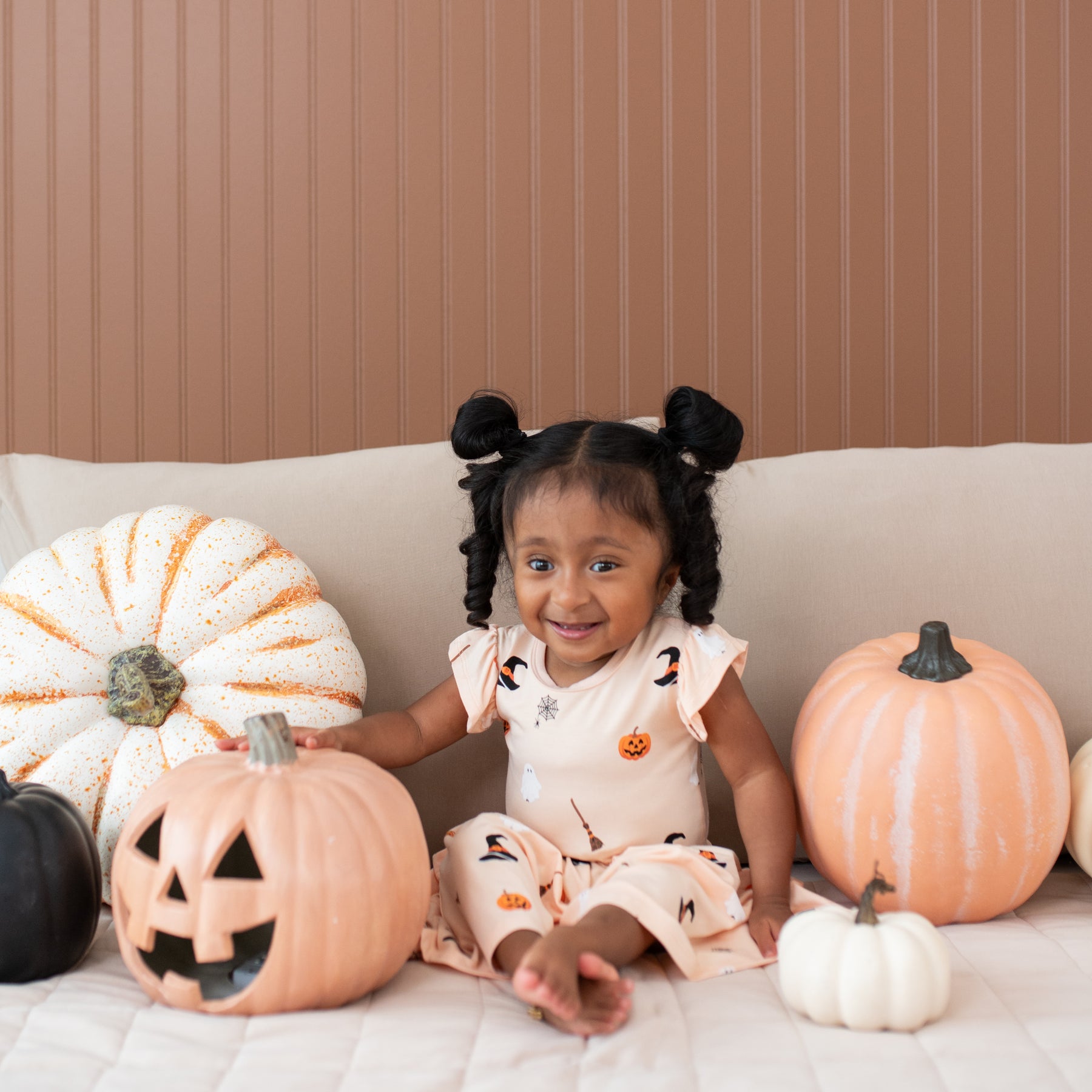 Child in a Halloween-themed pocket dress sitting on a couch with decorative pumpkins.