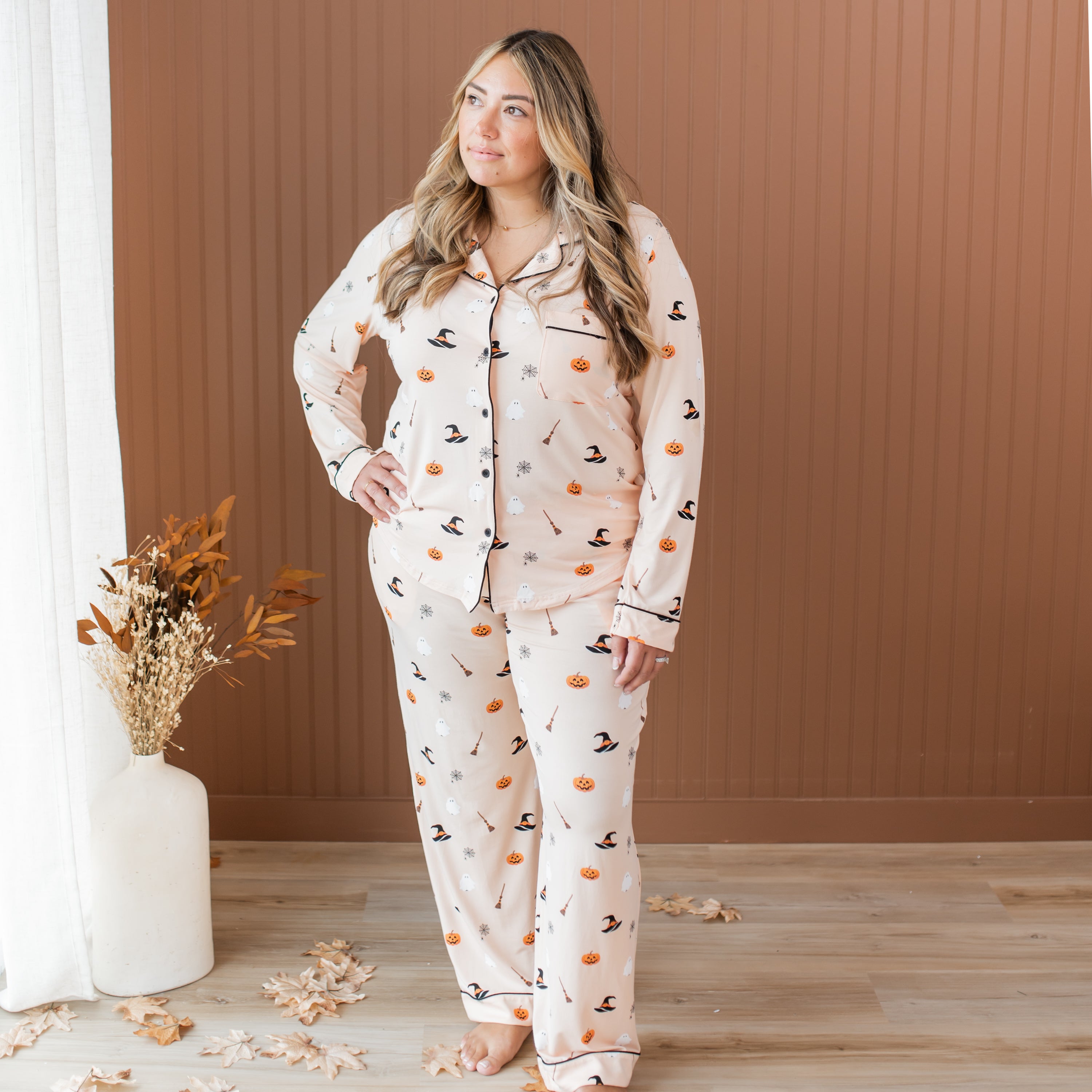 Woman wearing a Halloween-themed pajama set in a room with a wooden floor and brown wall.