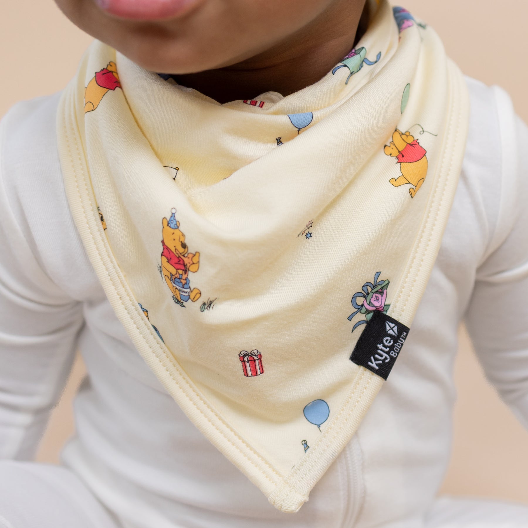 Close up of the Bib in Winnie the Pooh Celebration showing the black kyte baby logo tag on a toddler