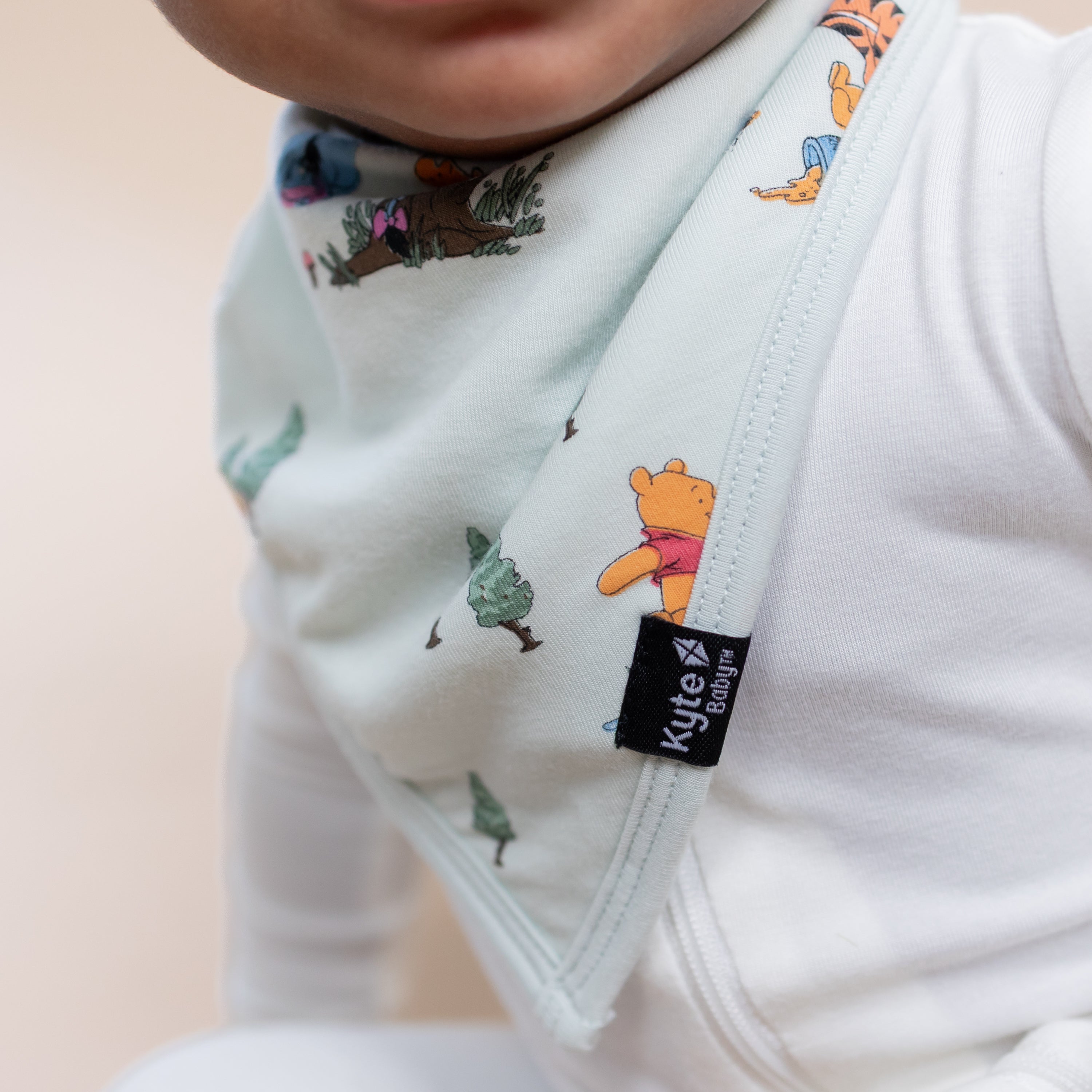 Close up of the Bib in Winnie the Pooh Hundred Acre Wood showing the black kyte baby logo shown on an infant