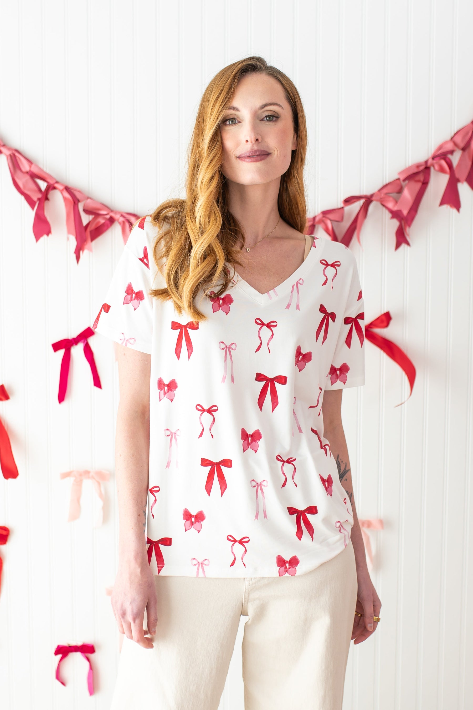 Woman standing in front of a streamer of bows while modeling the Bamboo Women's Relaxed Fit V-Neck in Big Love Bow