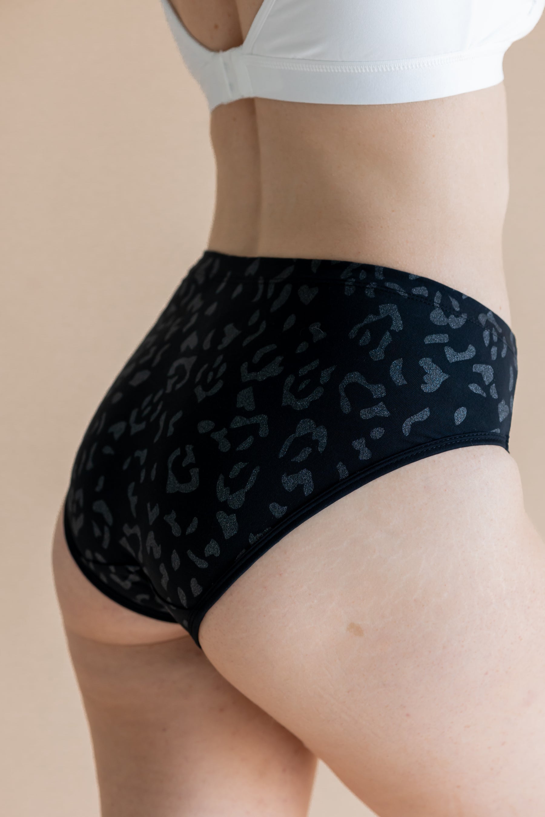Person wearing black leopard patterned underwear on a beige background