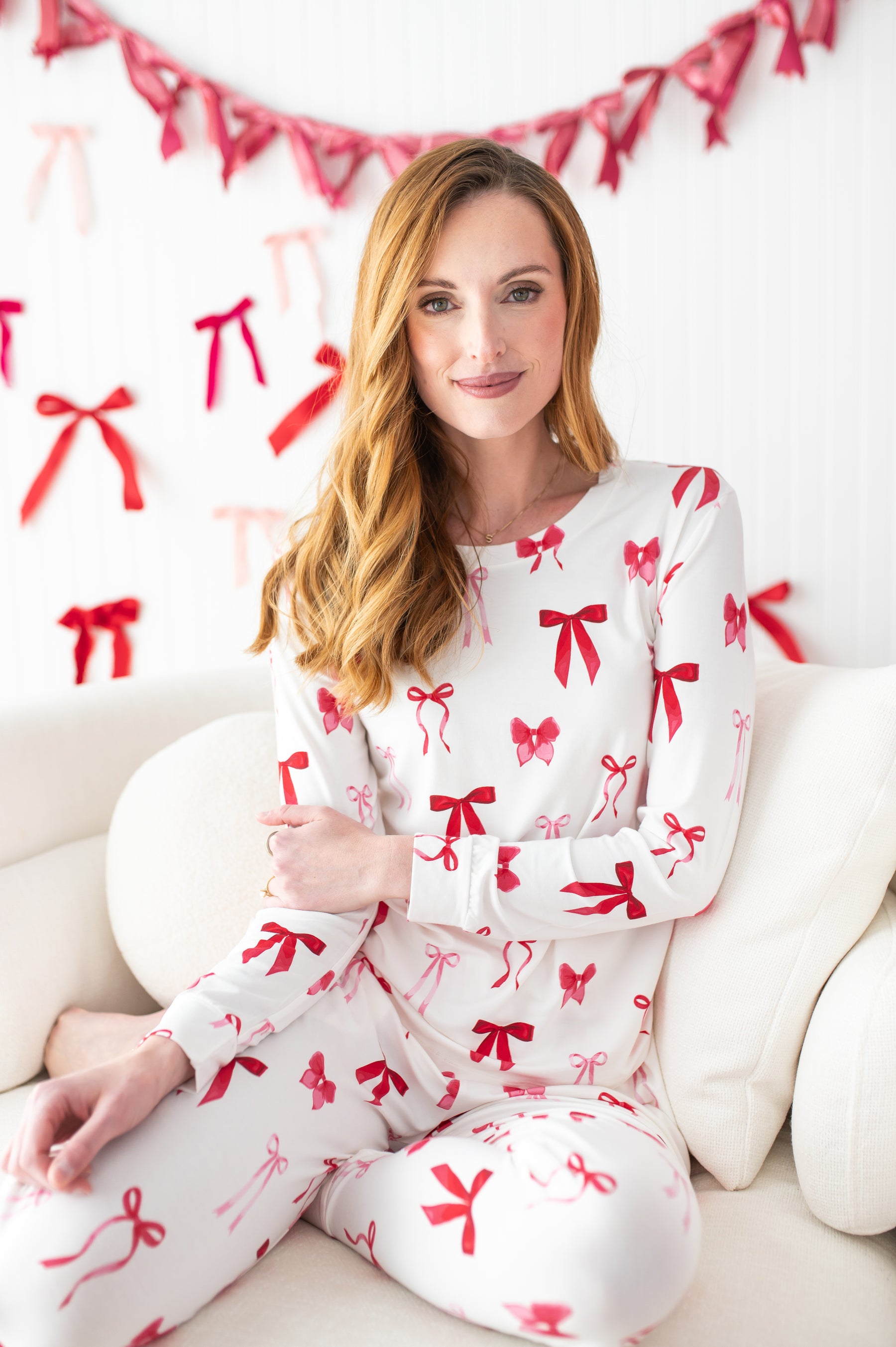 Female model sitting on a cream sofa wearing the soft and breathable Women's Jogger Pajama Set in Big Love Bow
