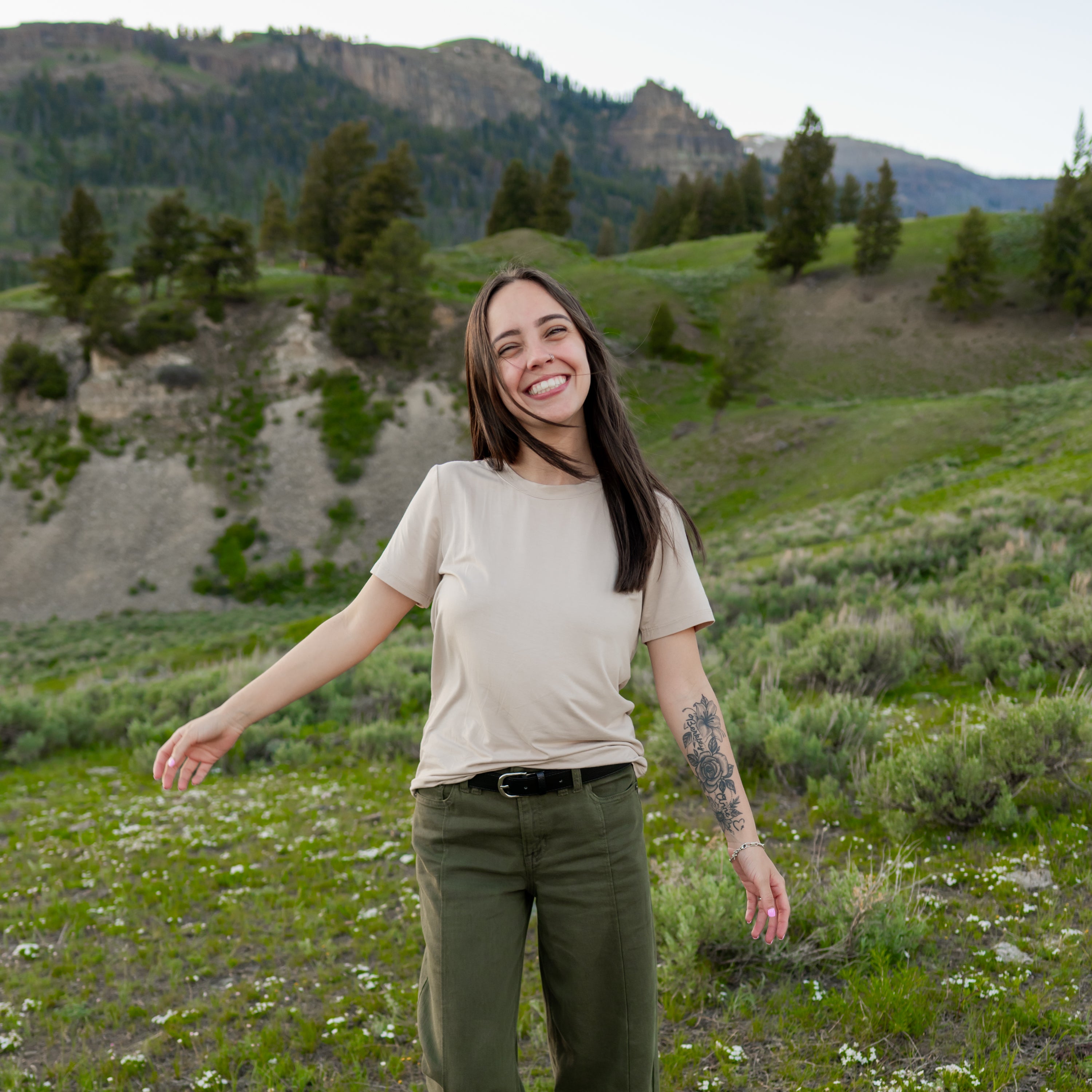 Smiling model walking through a field wearing the Women's Crew Neck Tee in Bisque and olive green pants