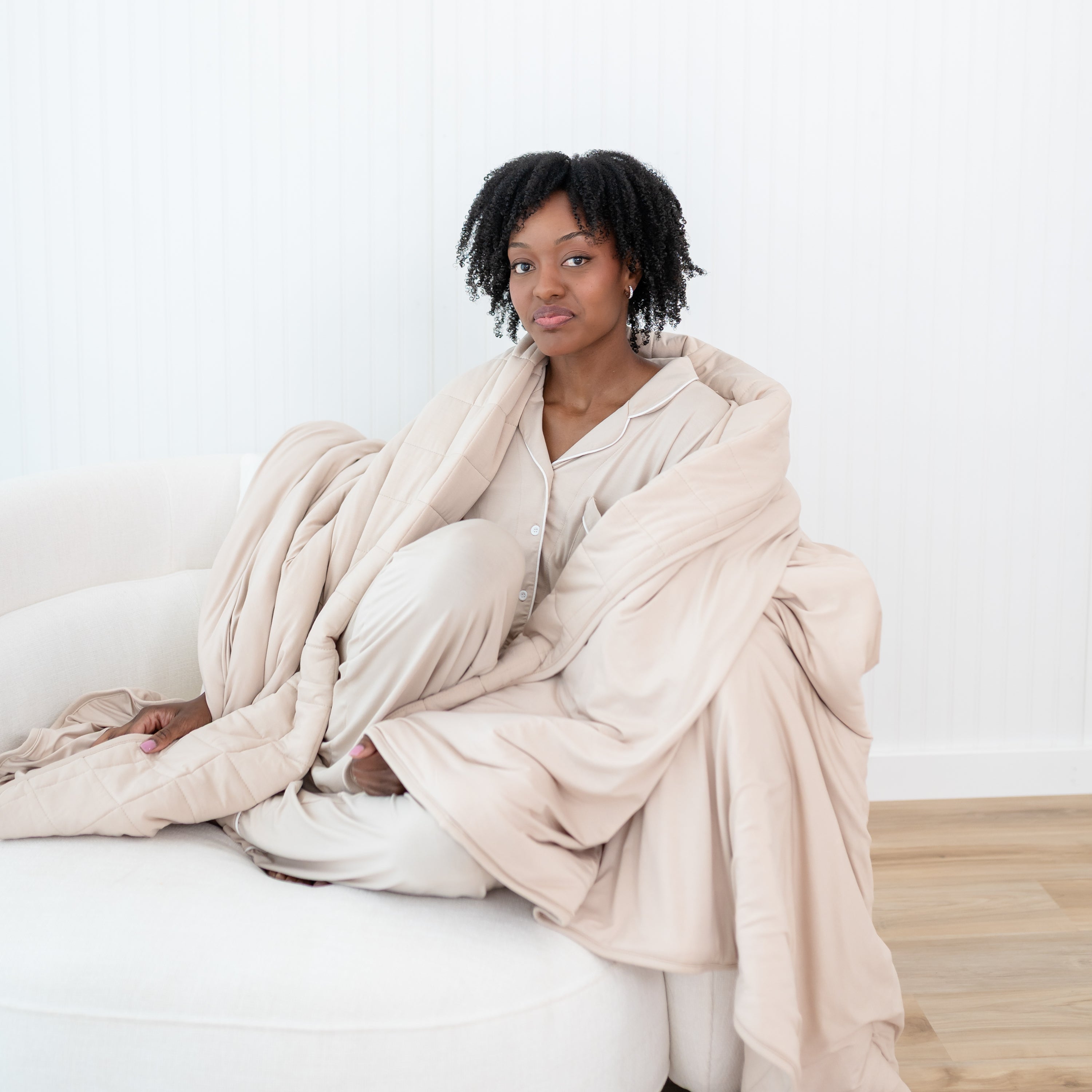 Female model sitting on the could with an Adult Quilted Blanket in Bisque 2.5 wearing matching women's long sleeve pajama set