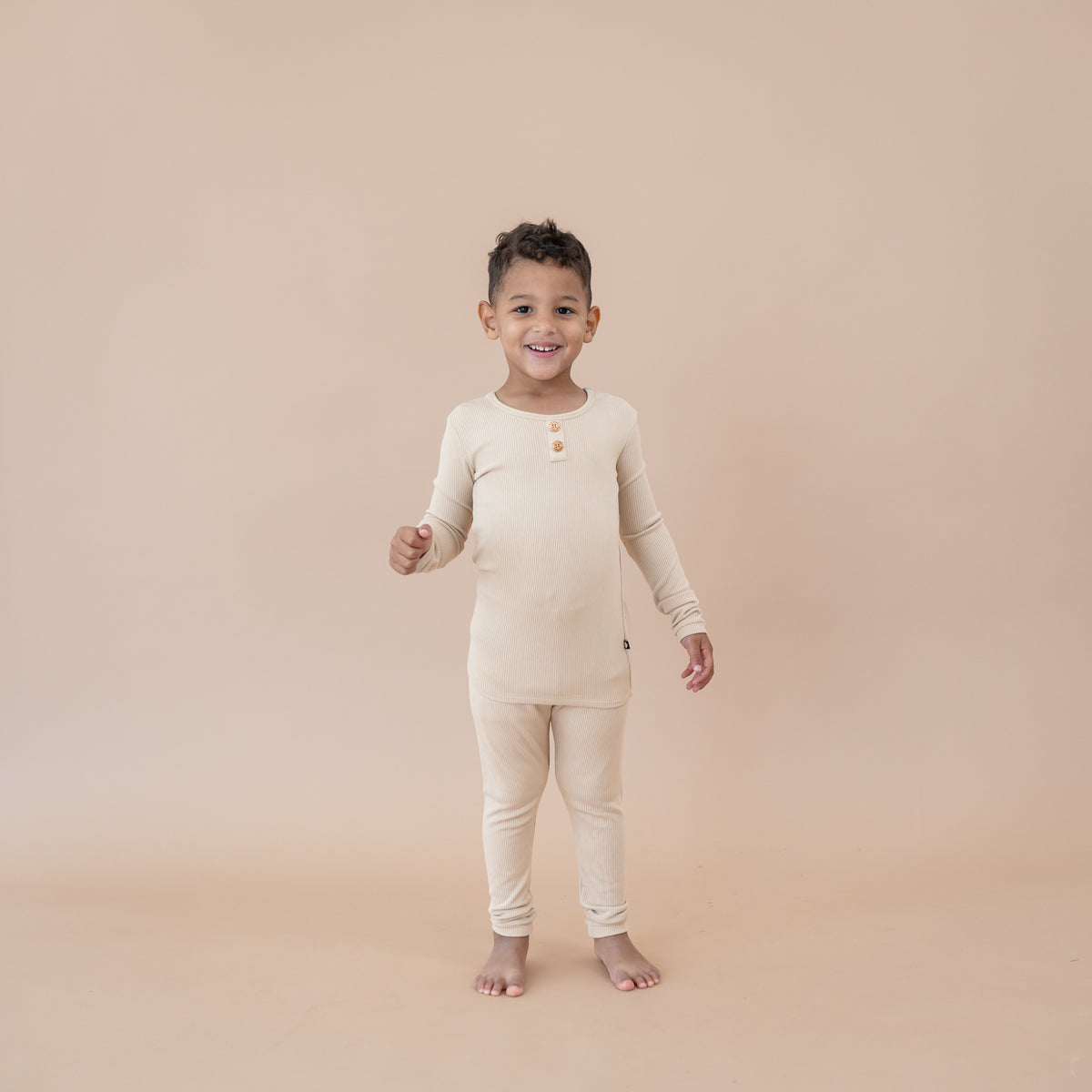 Young boy standing wearing the Ribbed Henley Set in Bisque in front of a taupe backdrop