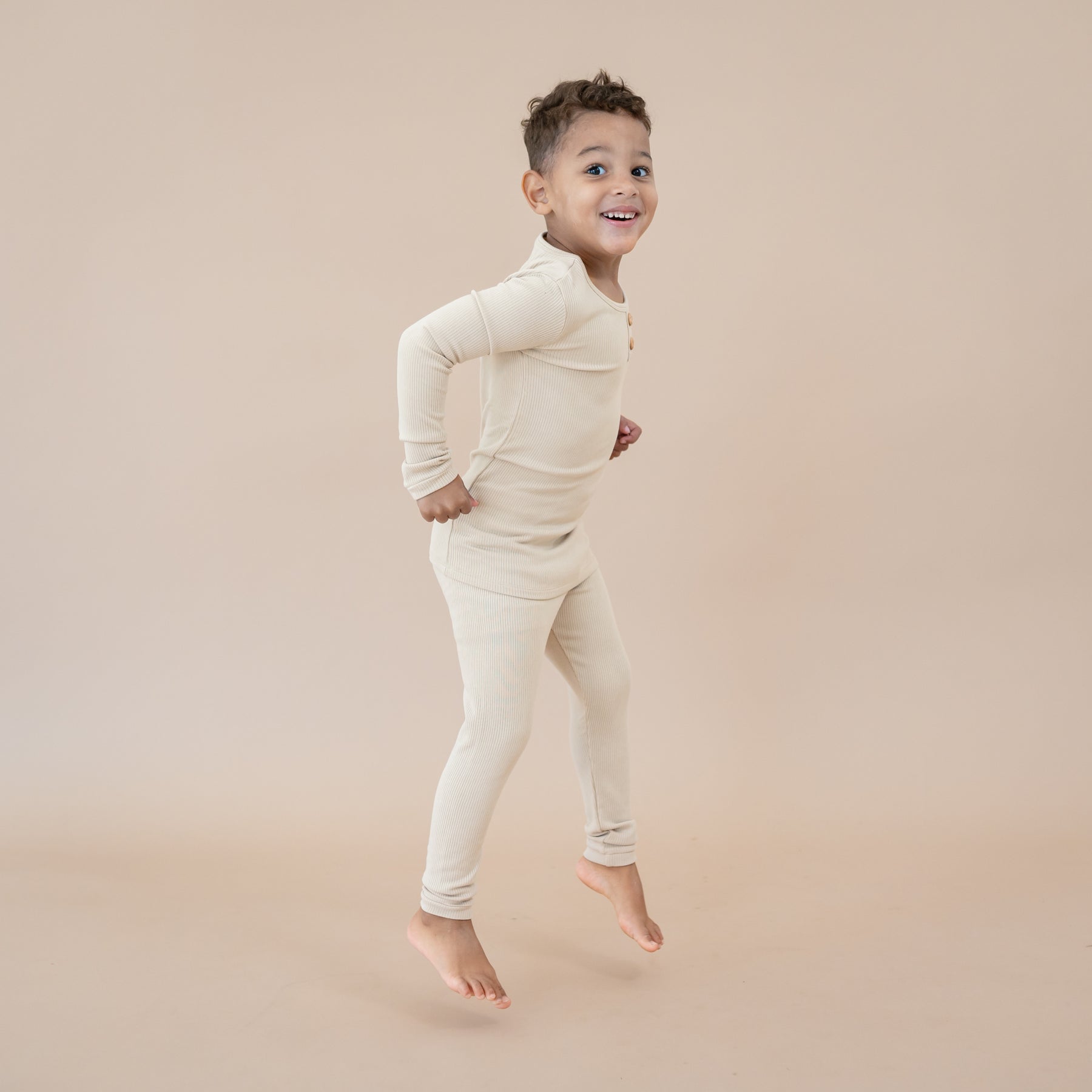 Young boy jumping in the Ribbed Henley Set in Bisque showing the side view of the set