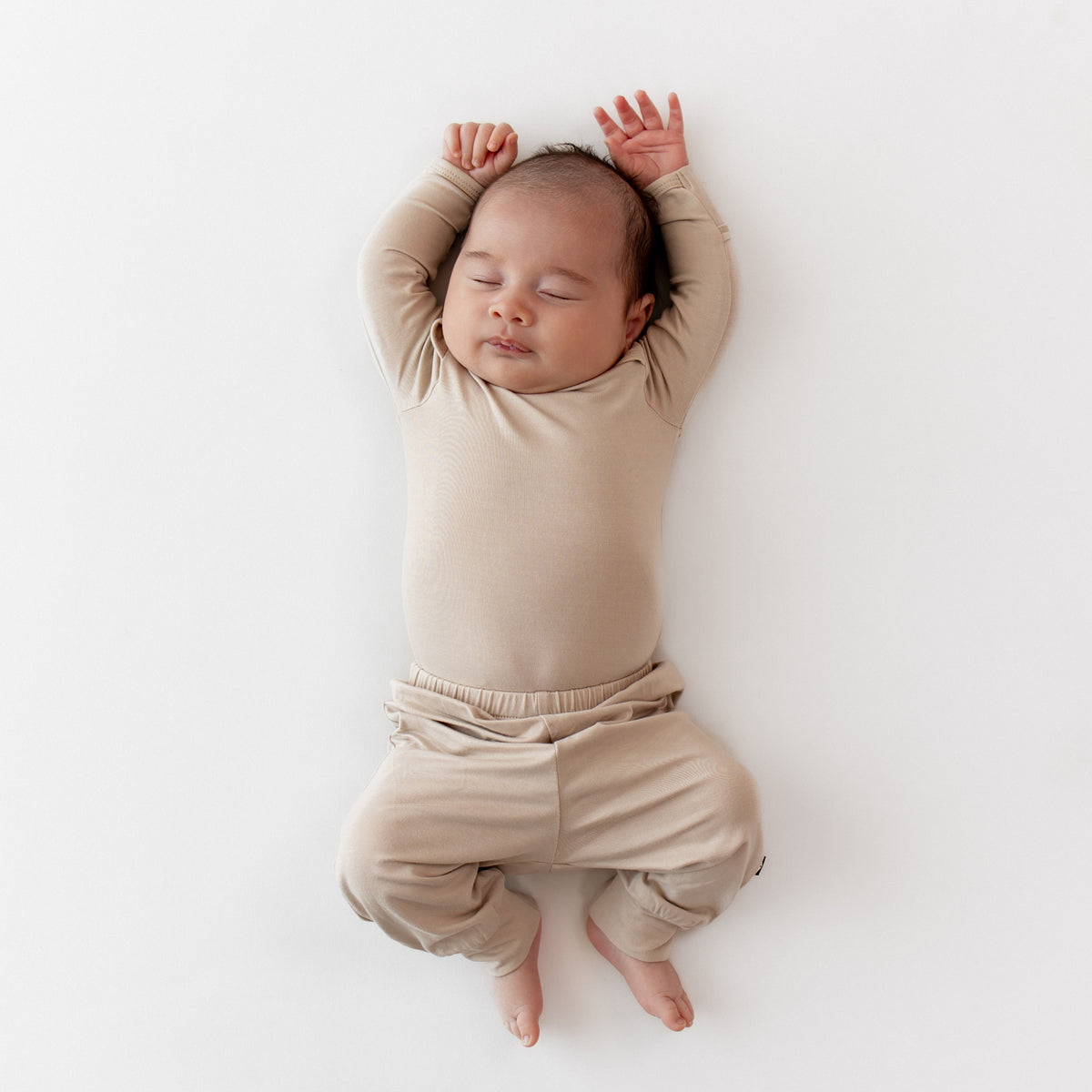 Sleeping newborn wearing the Pant in Bisque paired with a matching long sleeve bodysuit