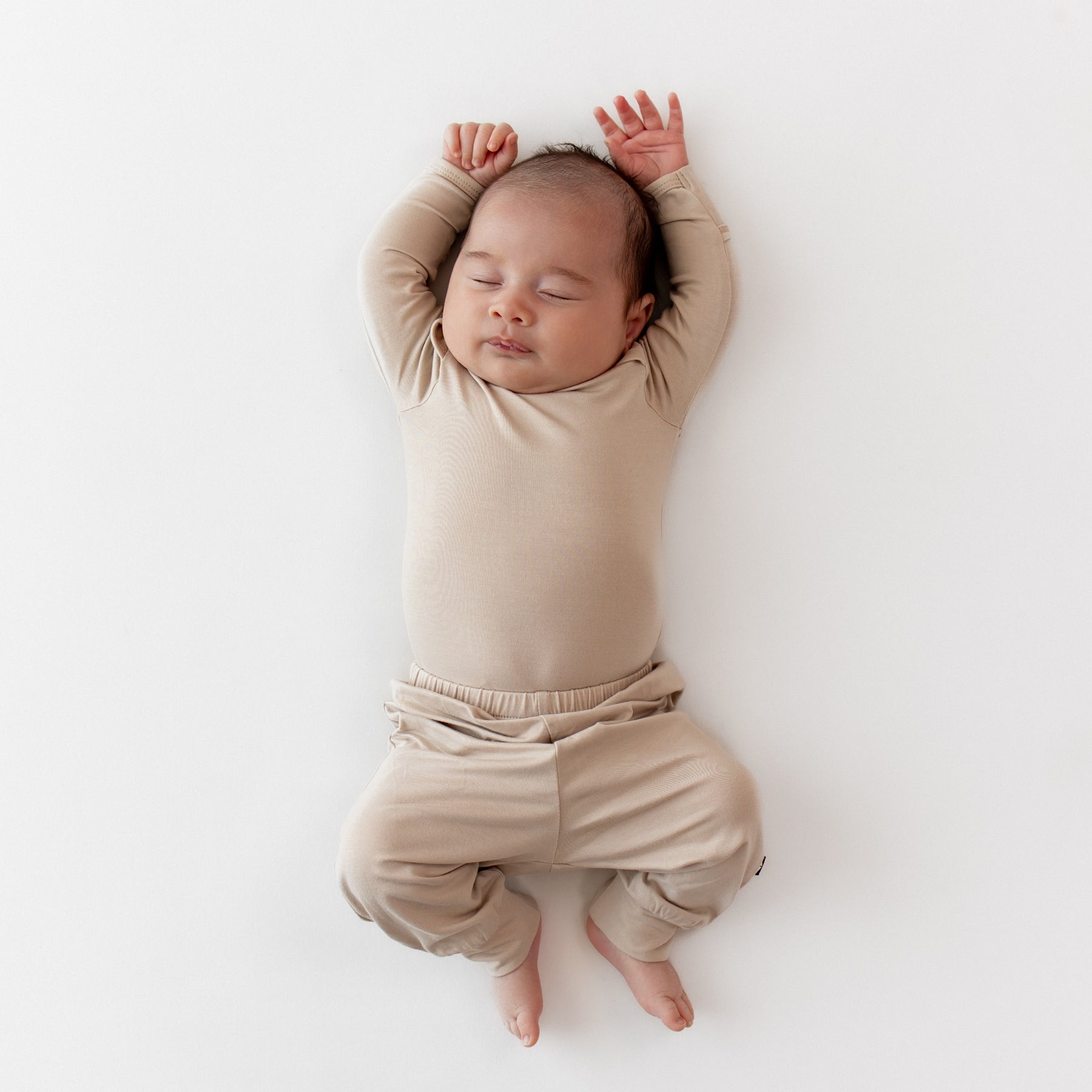 Sleeping newborn wearing the Pant in Bisque paired with a matching long sleeve bodysuit