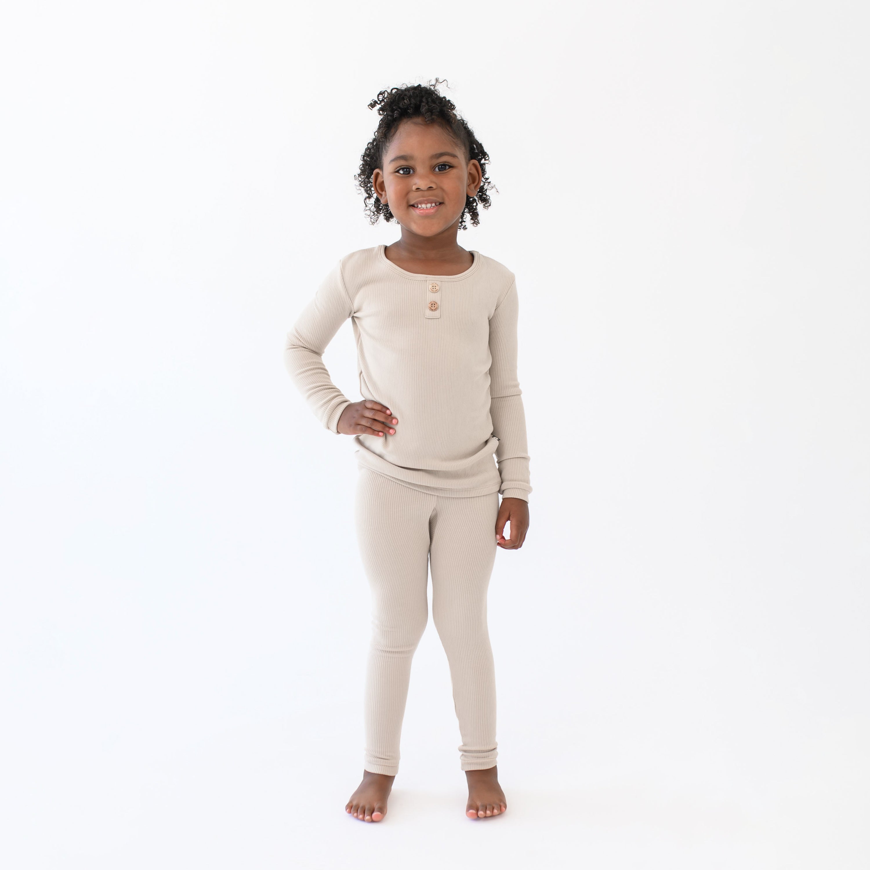 Young girl standing with one hand on her hip wearing the Ribbed Henley Set in Bisque in front of a white back drop