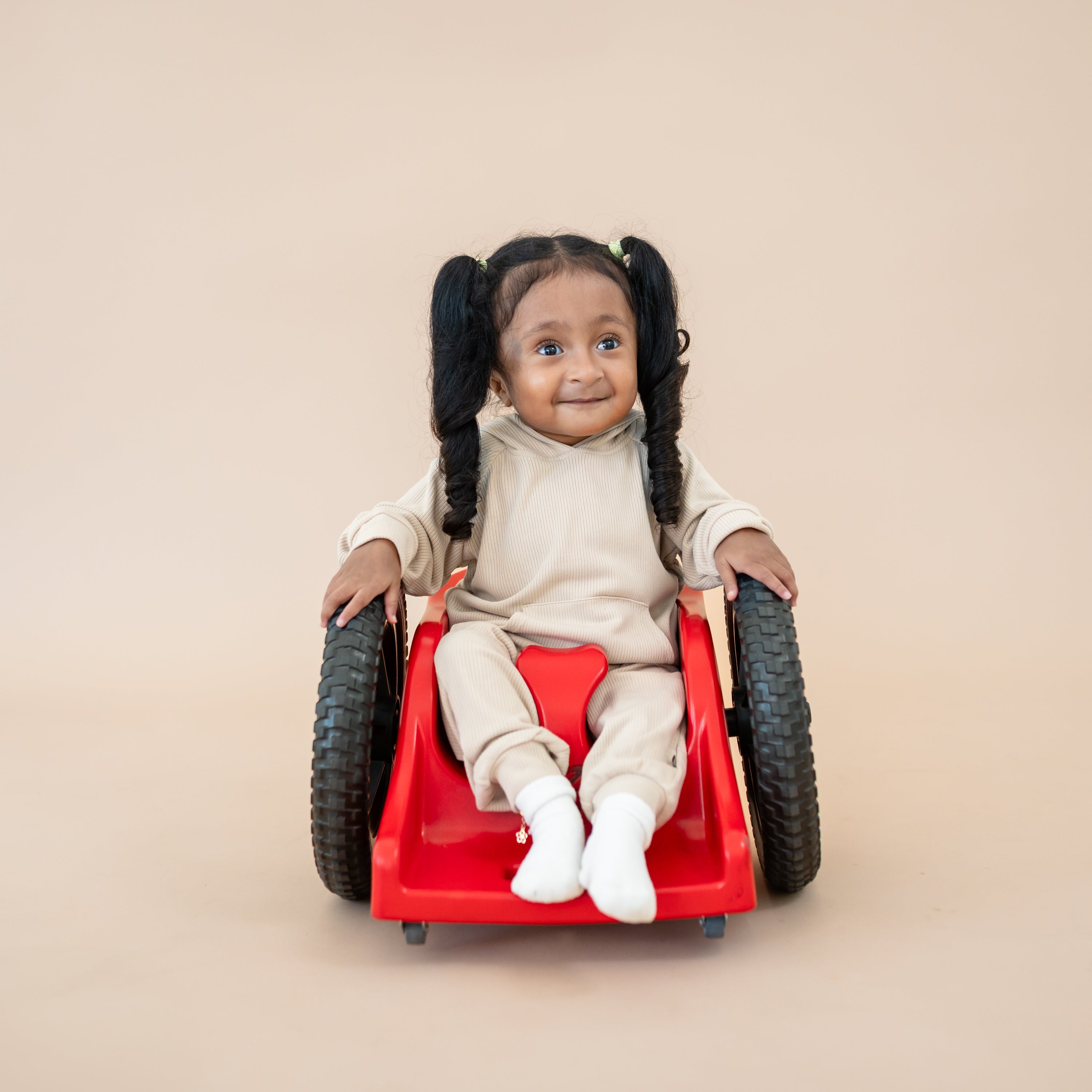 Young girl sitting in her red wheelchair with her hands on the wheels wearing the Ribbed Hoodie in Bisque and matching ribbed jogger pants