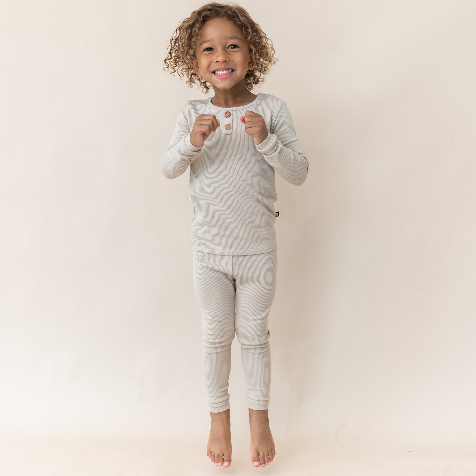 Young girl jumping wearing the Ribbed Henley Set in Bisque
