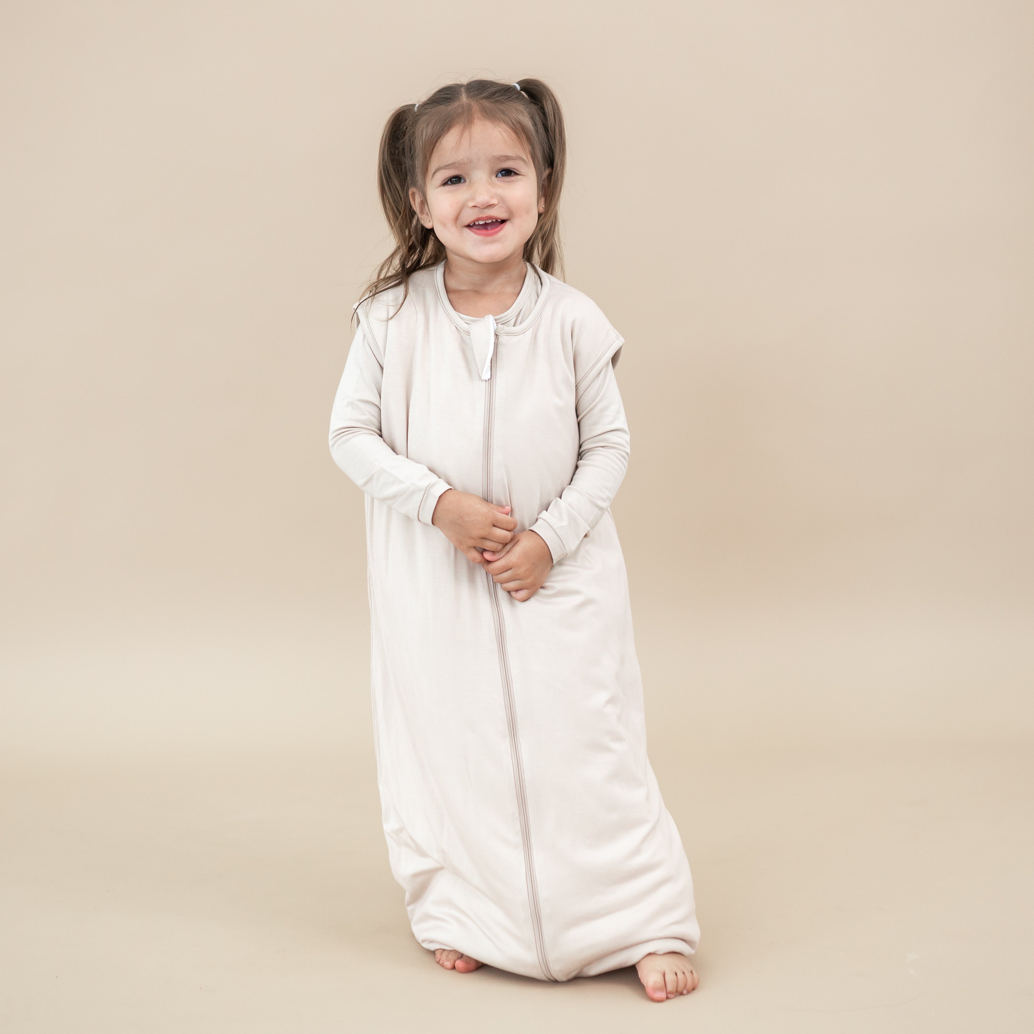 Smiling young girl wearing the Sleep Bag Walker in Bisque 1.0 with matching long sleeve pajamas on undereath