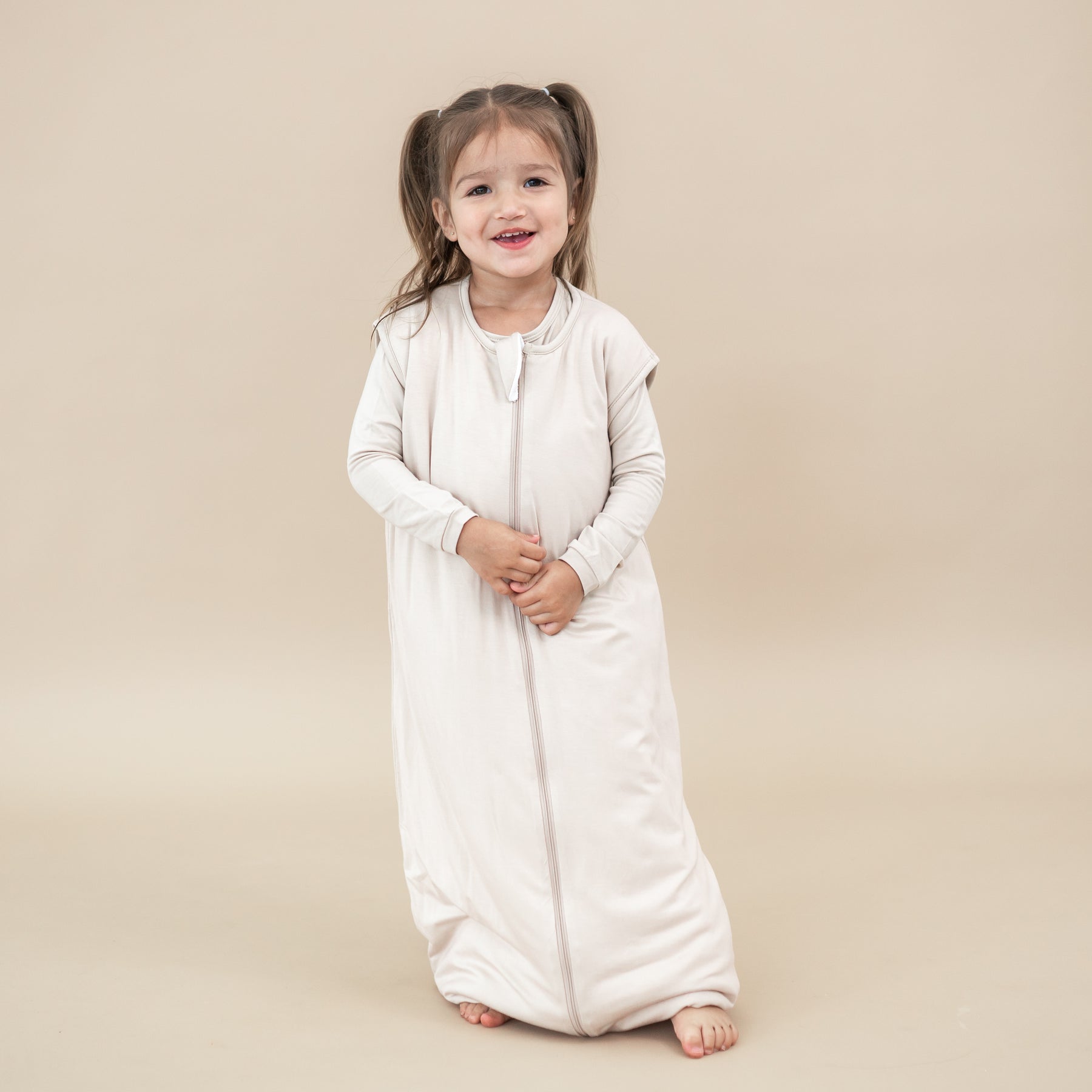 Smiling young girl wearing the Sleep Bag Walker in Bisque 1.0 with matching long sleeve pajamas on undereath
