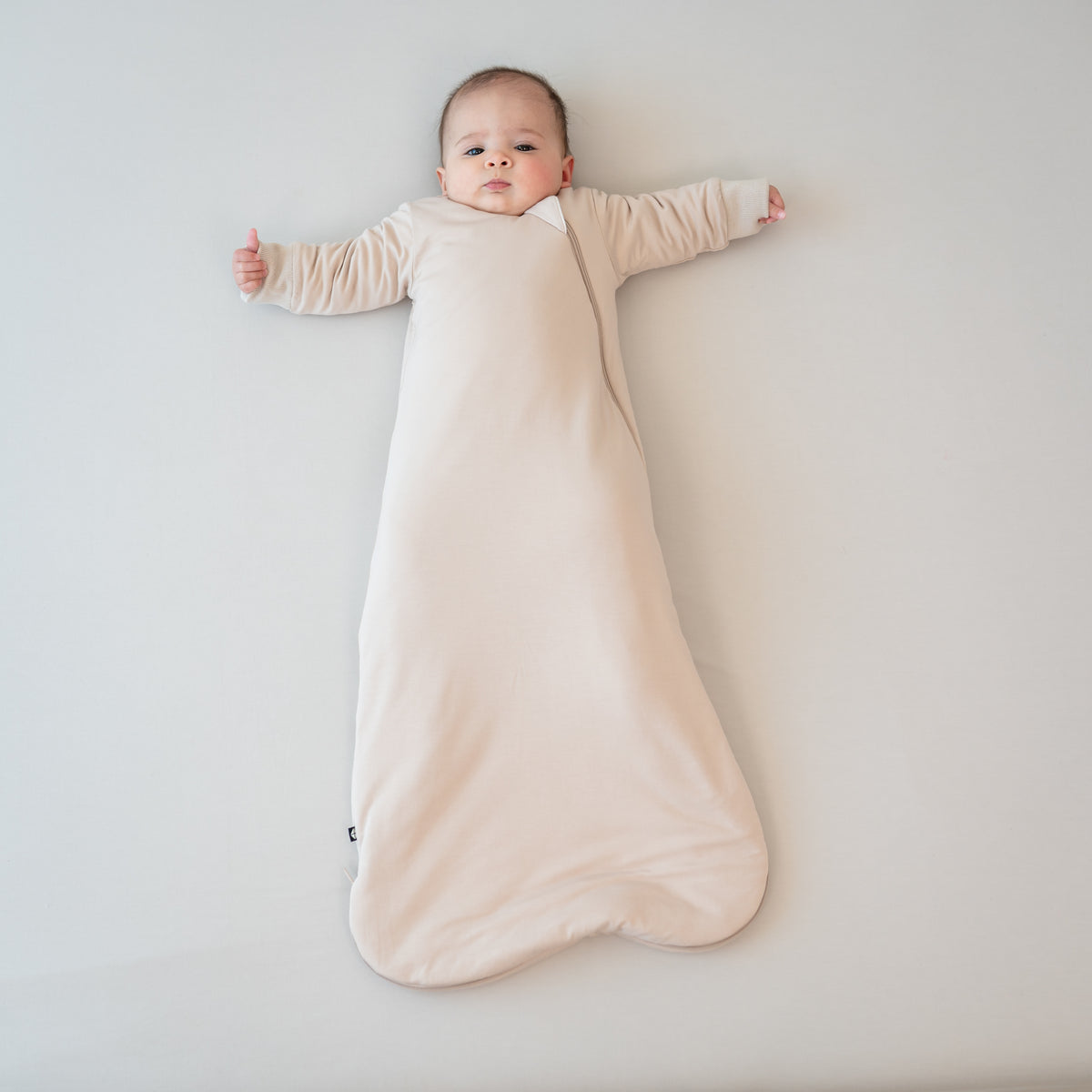 Infant laying down wearing the Slumber Bag in Bisque