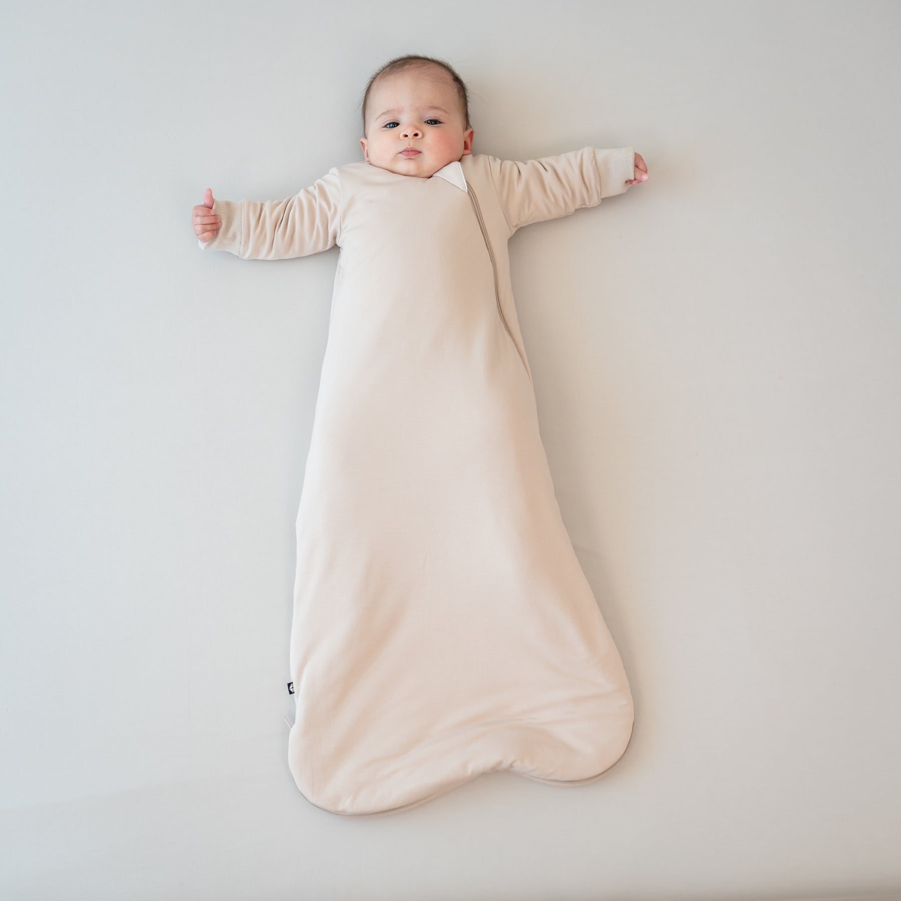 Infant laying down wearing the Slumber Bag in Bisque