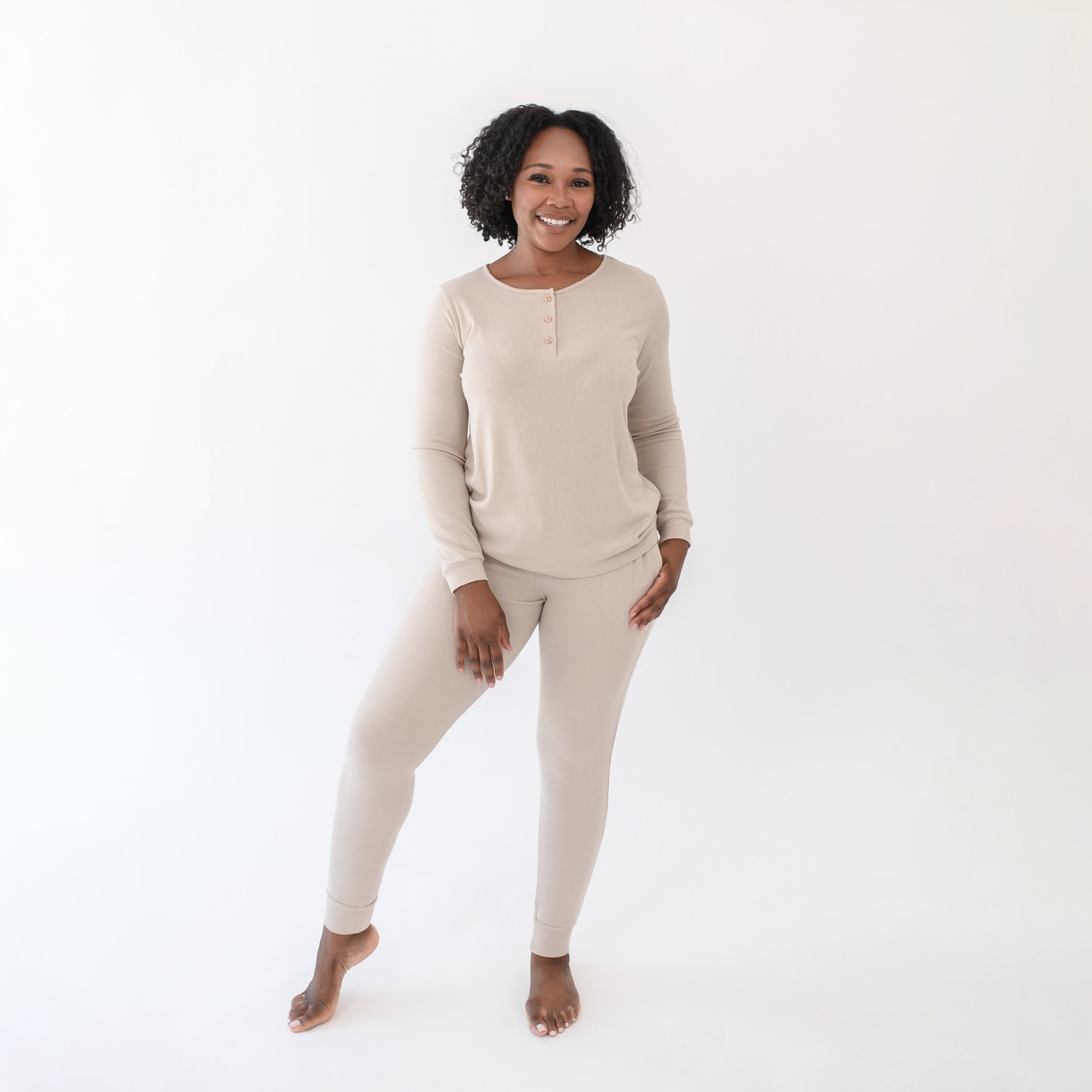 Smiling female standing in front of a white back drop wearing the Women’s Ribbed Henley Set in Bisque