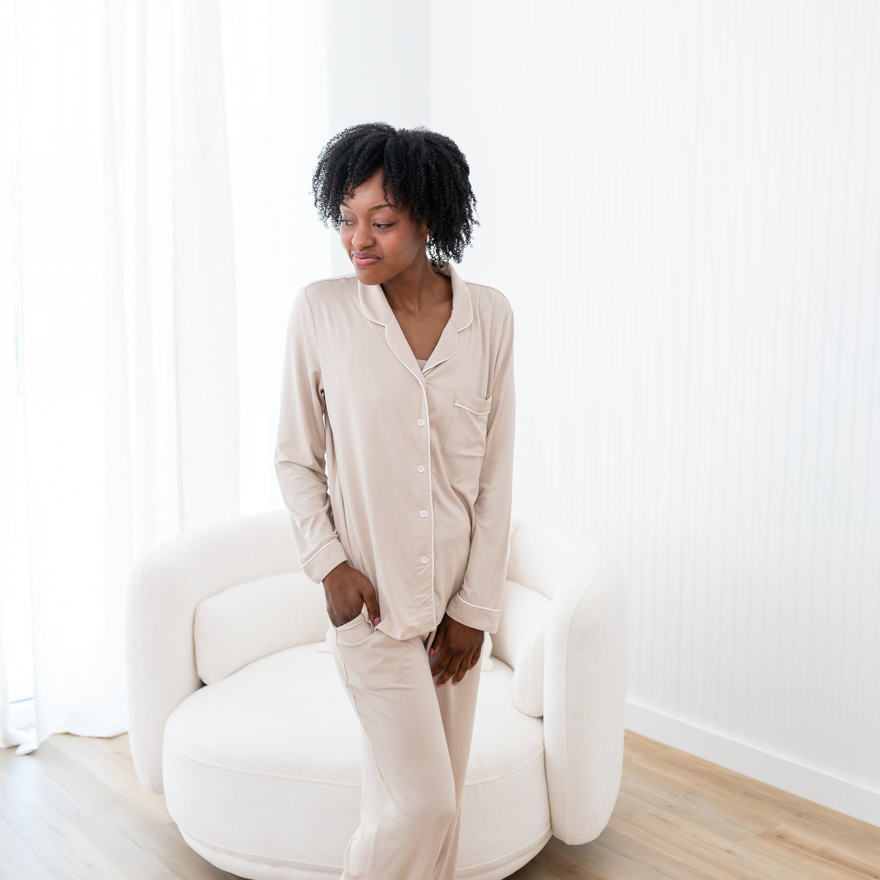 Female model standing in front of a sofa wearing the Long-Sleeved Women's Pajama Set in Bisque with Cloud Trim