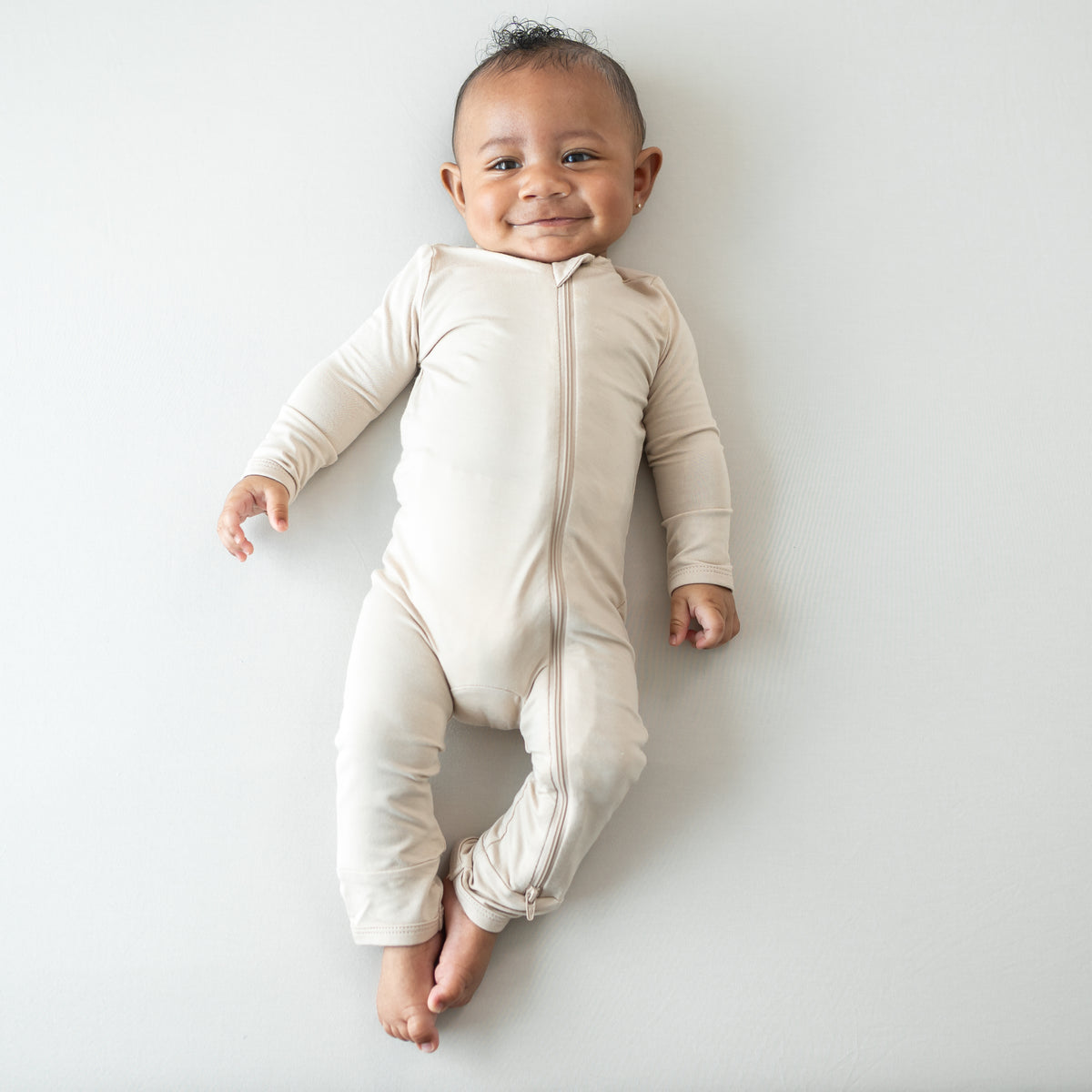 Smiling infant wearing the Zippered Romper in Bisque
