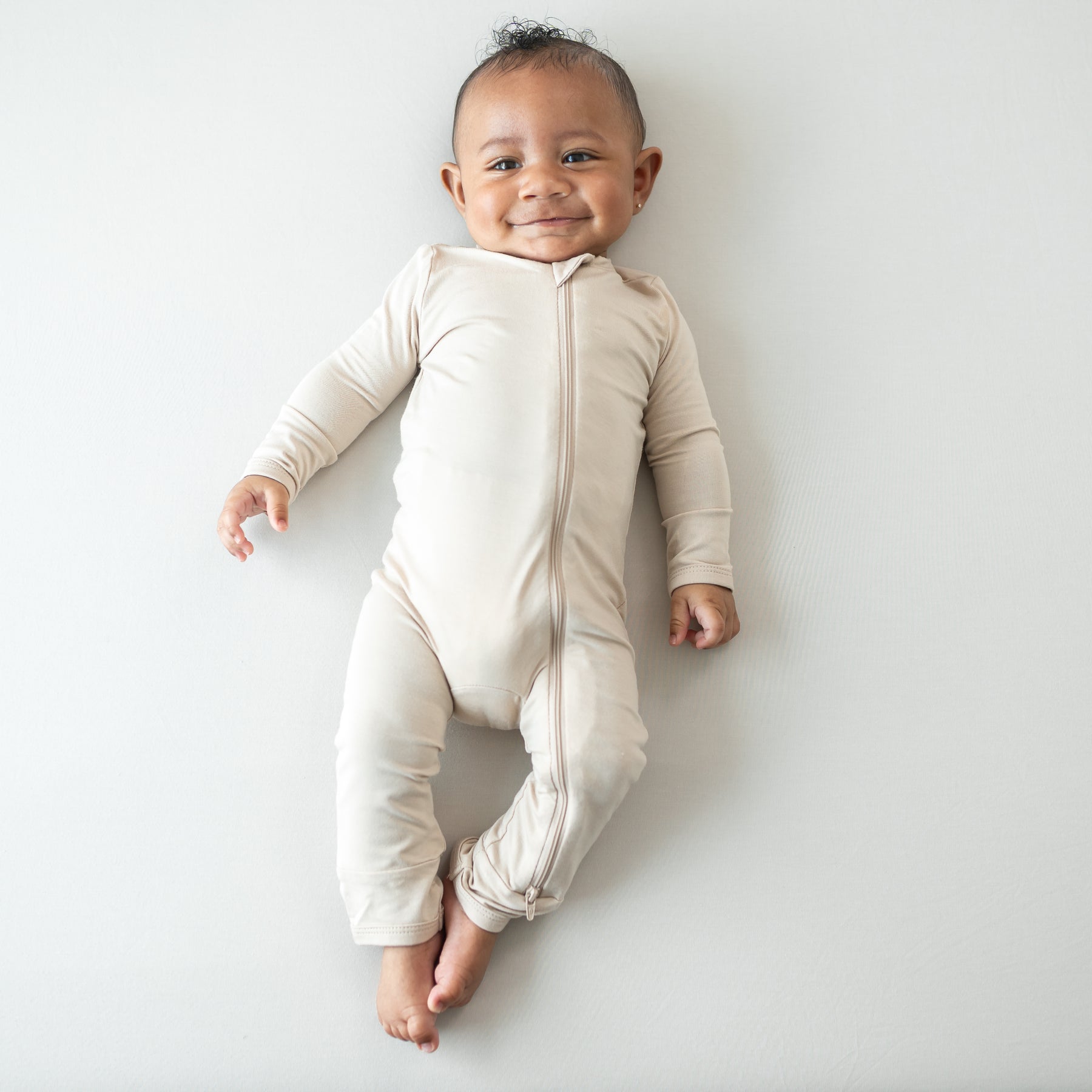 Smiling infant wearing the Zippered Romper in Bisque