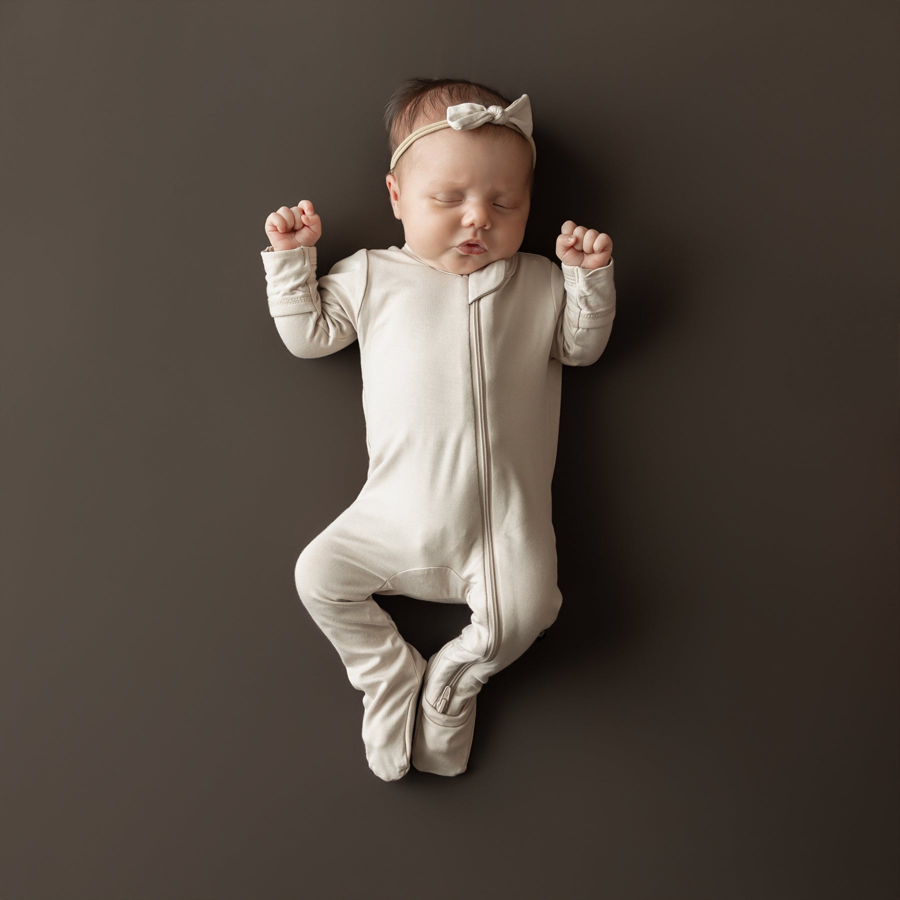 Sleeping newborn with arms up wearing the Zippered Footie in Bisque