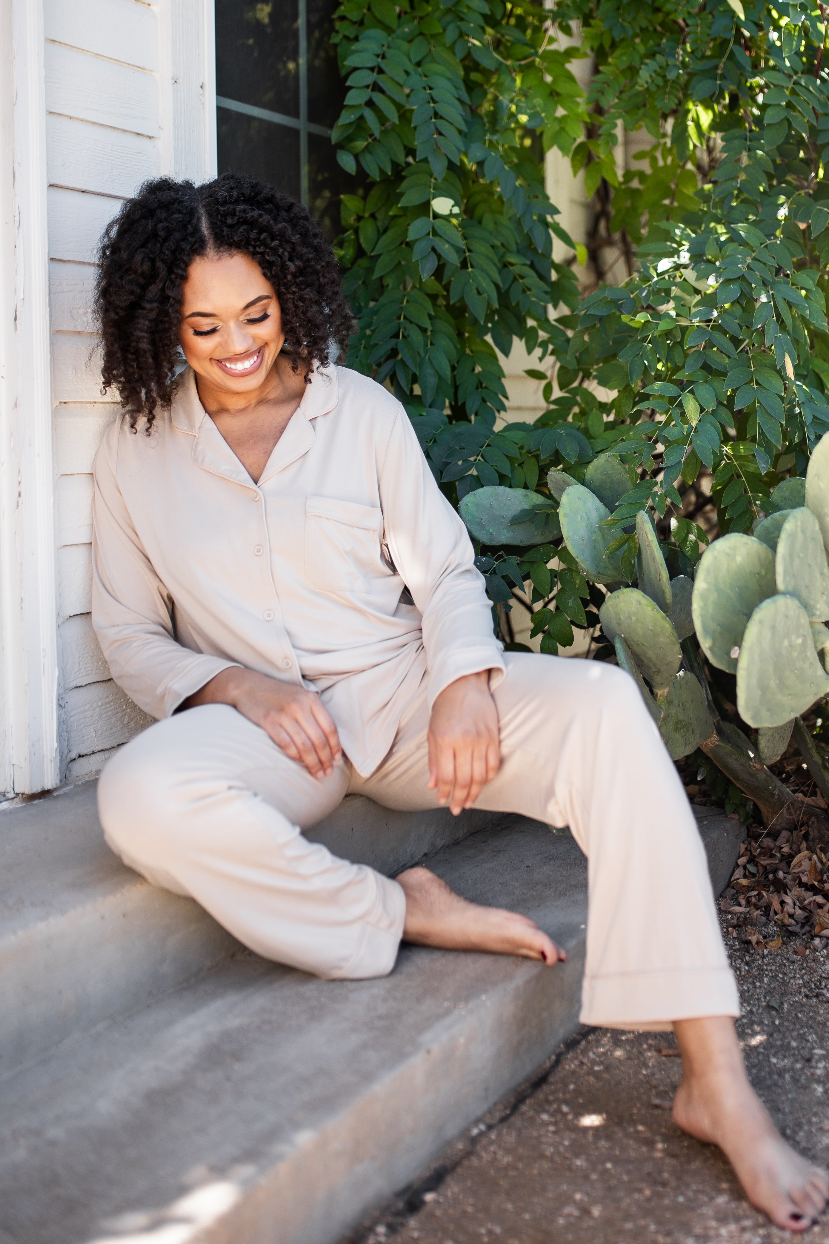 Smiling female sitting on concrete steps wearing the Long-Sleeved Women's Pajama Set in Bisque with Bisque Trim