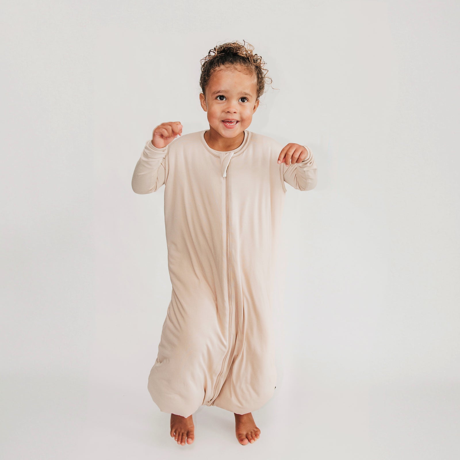 Young kid jumping wearing the Sleep Bag Walker in Bisque 2.5 and matching long sleeve toddler pajamas on underneath