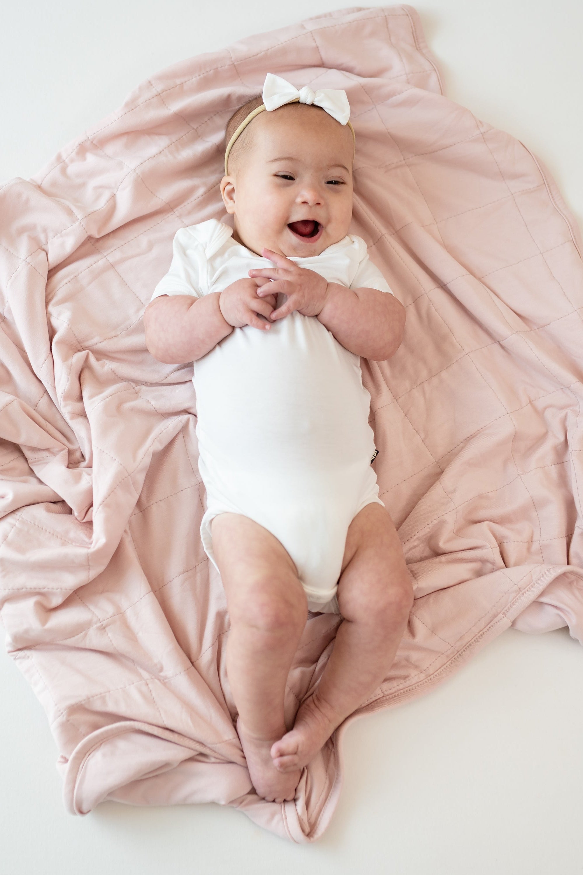 Baby wearing a Cloud Bodysuit laying on Baby Blanket in Blush 1.0