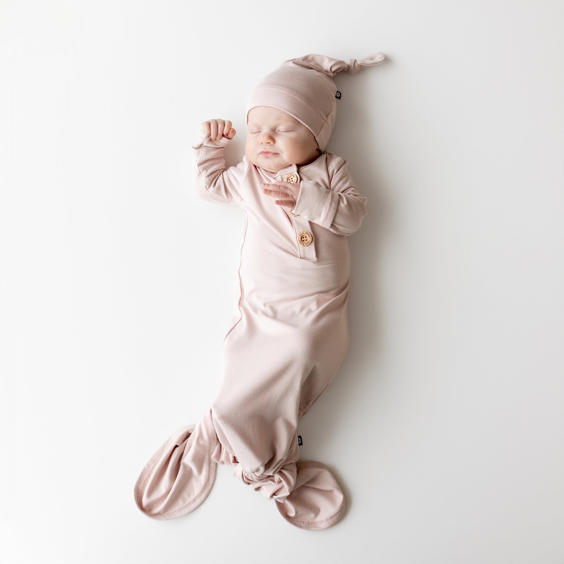 Newborn baby in a pink knotted gown and hat on a white background