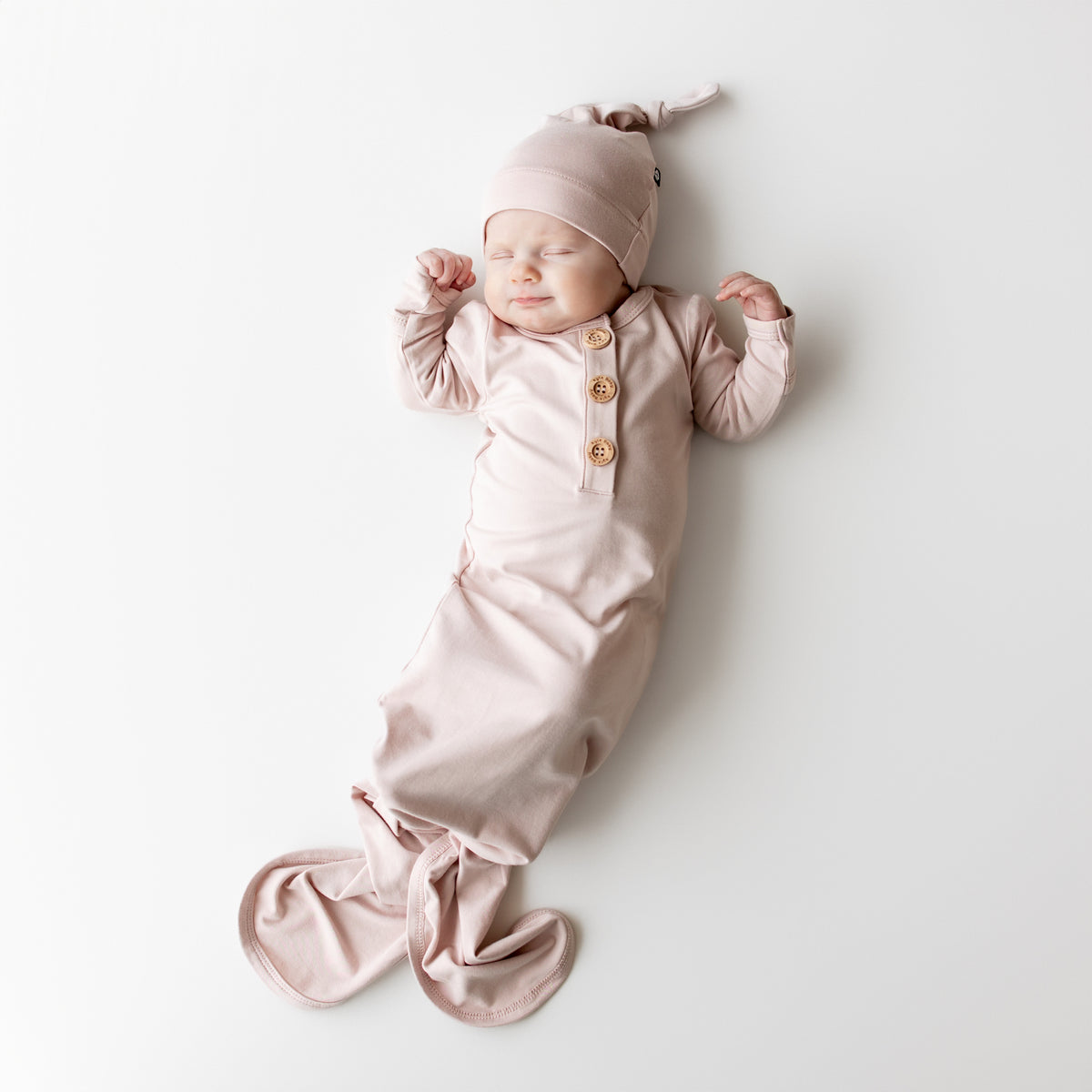 Newborn baby in a pink knotted gown and hat lying on a white background