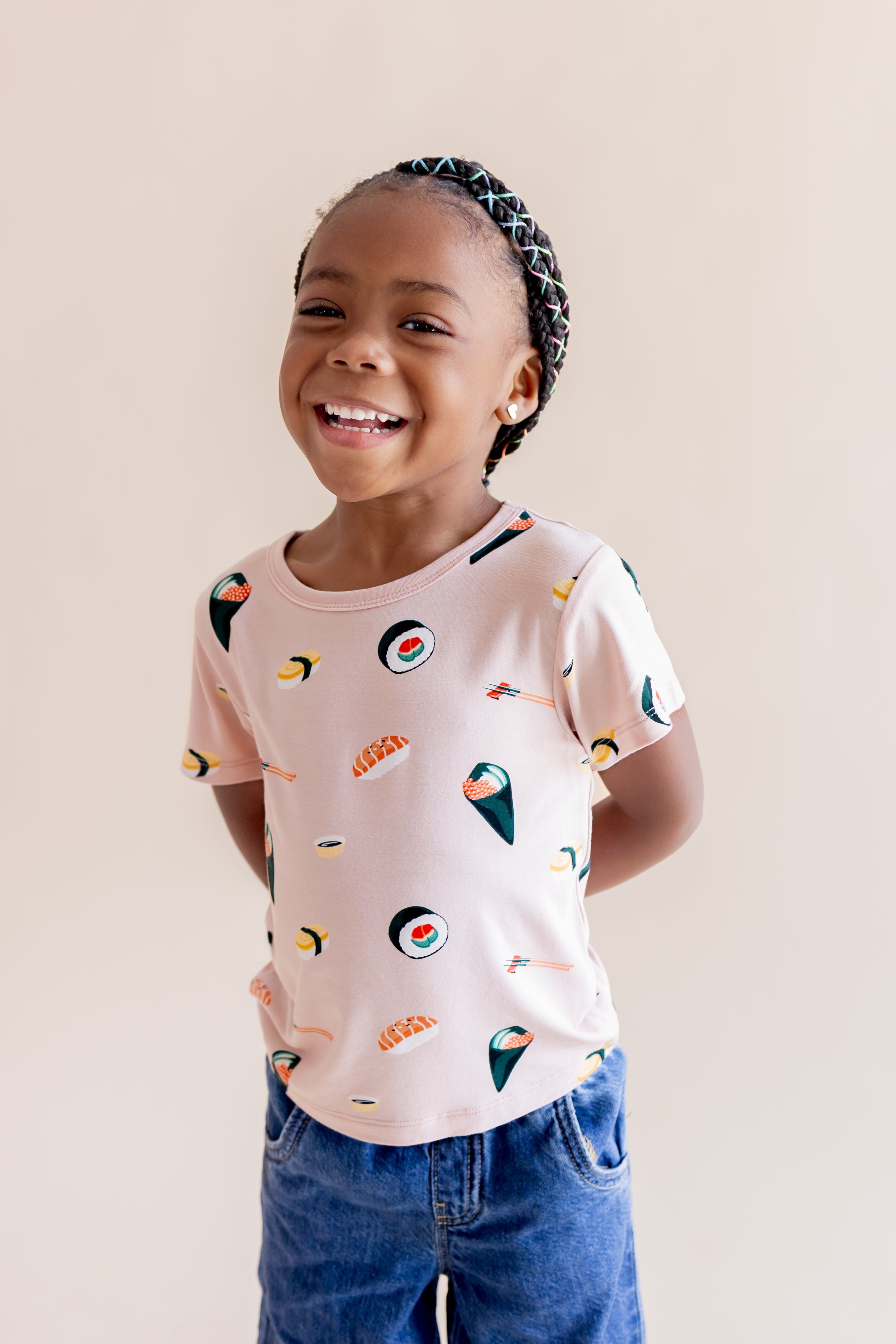 Child standing and smiling wearing blush sushi tee with jeans